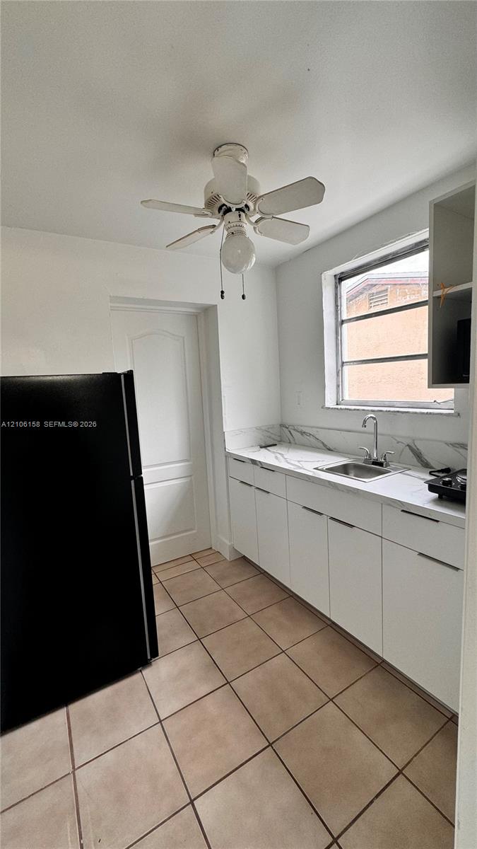 Kitchen featuring flat-panel white cabinetry, stone-patterned backsplash, square tile flooring, and ceiling fan with integrated lighting Kitchen featuring flat-panel white cabinetry, stone-patterned backsplash, square tile flooring, and ceiling fan with integrated lighting