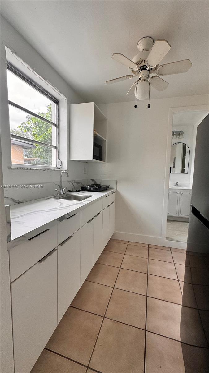 White cabinetry with minimalist hardware, stone-finish countertops, stainless steel undermount sink, multi-pane window, and ceramic tile flooring White cabinetry with minimalist hardware, stone-finish countertops, stainless steel undermount sink, multi-pane window, and ceramic tile flooring