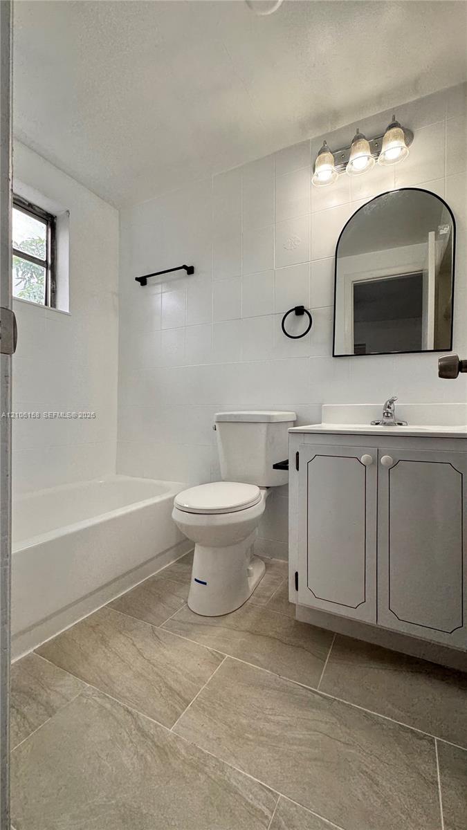 Bathroom featuring tile flooring, a white vanity cabinet with a neutral countertop, an arched wall-mounted mirror, and a three-light vanity fixture Bathroom featuring tile flooring, a white vanity cabinet with a neutral countertop, an arched wall-mounted mirror, and a three-light vanity fixture