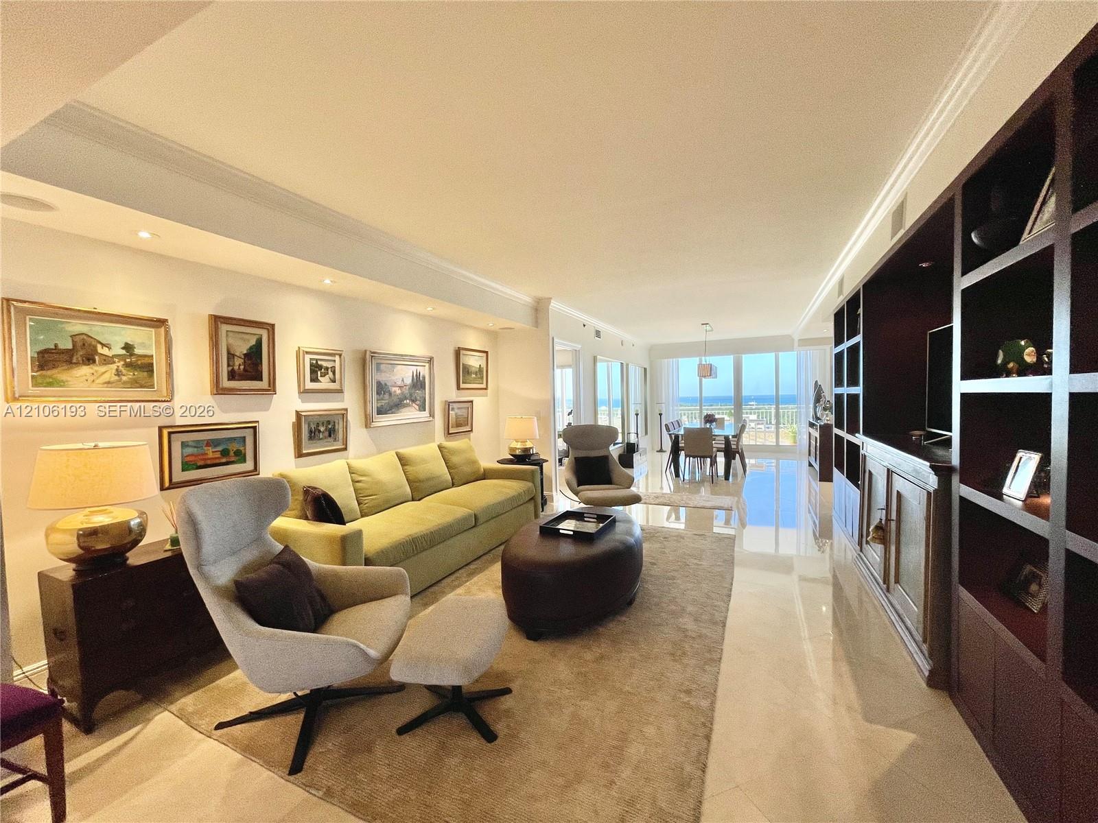 Open-concept living space featuring large-format polished stone flooring, custom floor-to-ceiling dark wood built-in cabinetry, recessed perimeter lighting, and expansive glass sliding doors