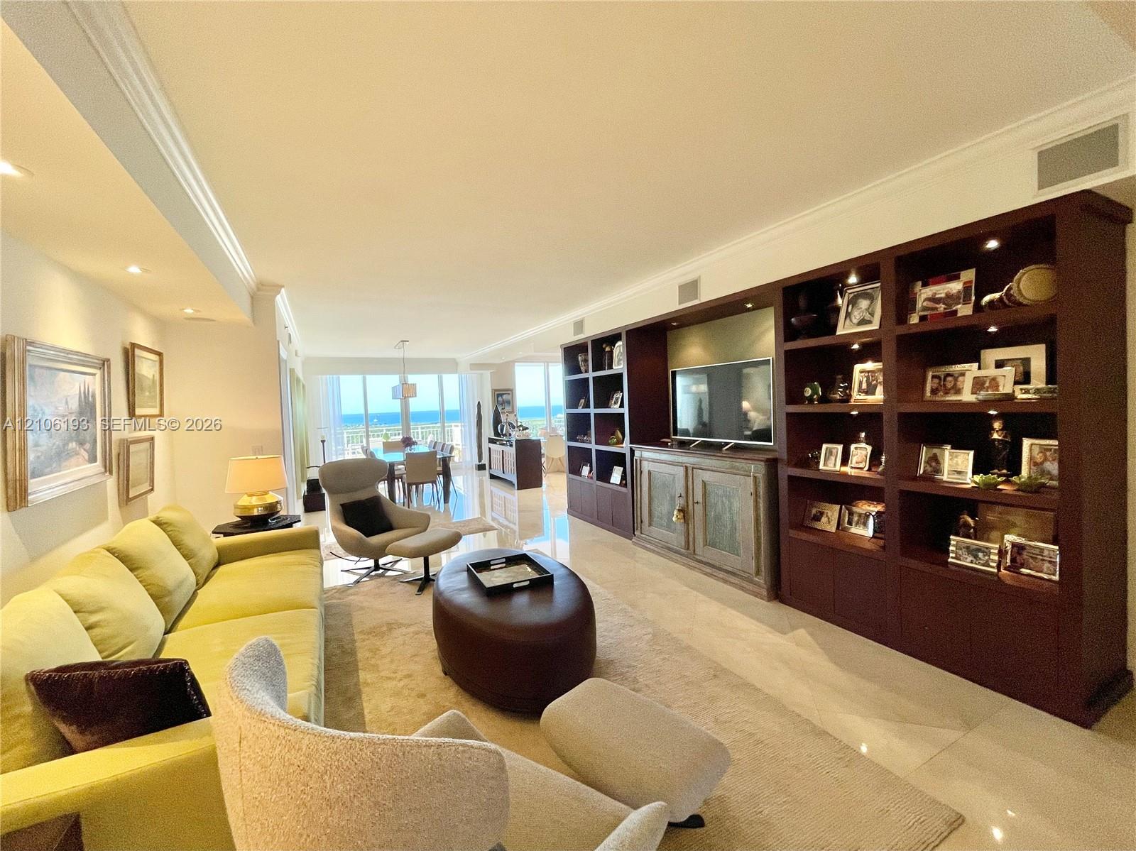 Large living area featuring polished stone flooring, extensive built-in floor-to-ceiling dark wood shelving, recessed lighting, and floor-to-ceiling windows