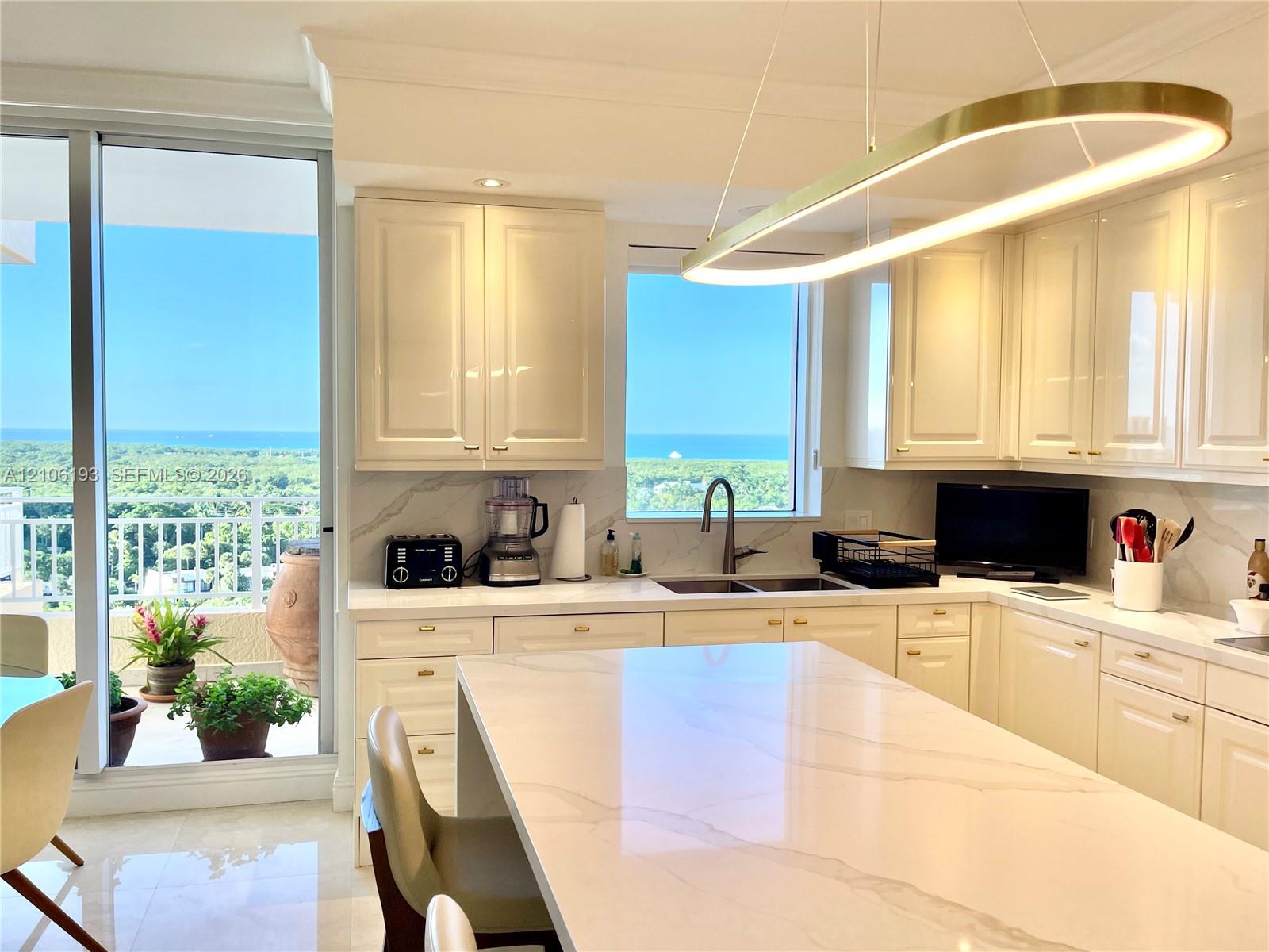 Kitchen featuring glossy cream cabinetry, a central island with a stone countertop, an integrated stainless steel dual-basin sink, and a circular LED pendant light fixture