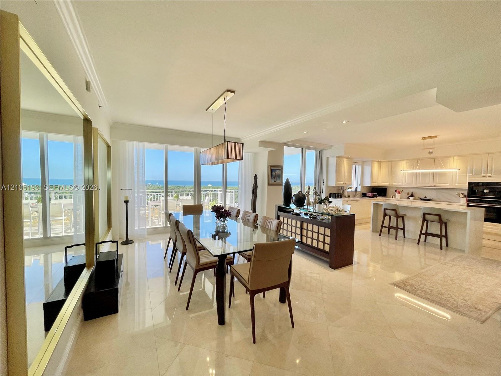 Open-concept living space featuring polished tile flooring, floor-to-ceiling glass sliding doors, custom white cabinetry, a built-in kitchen island with stone-finish countertops, and recessed lighting