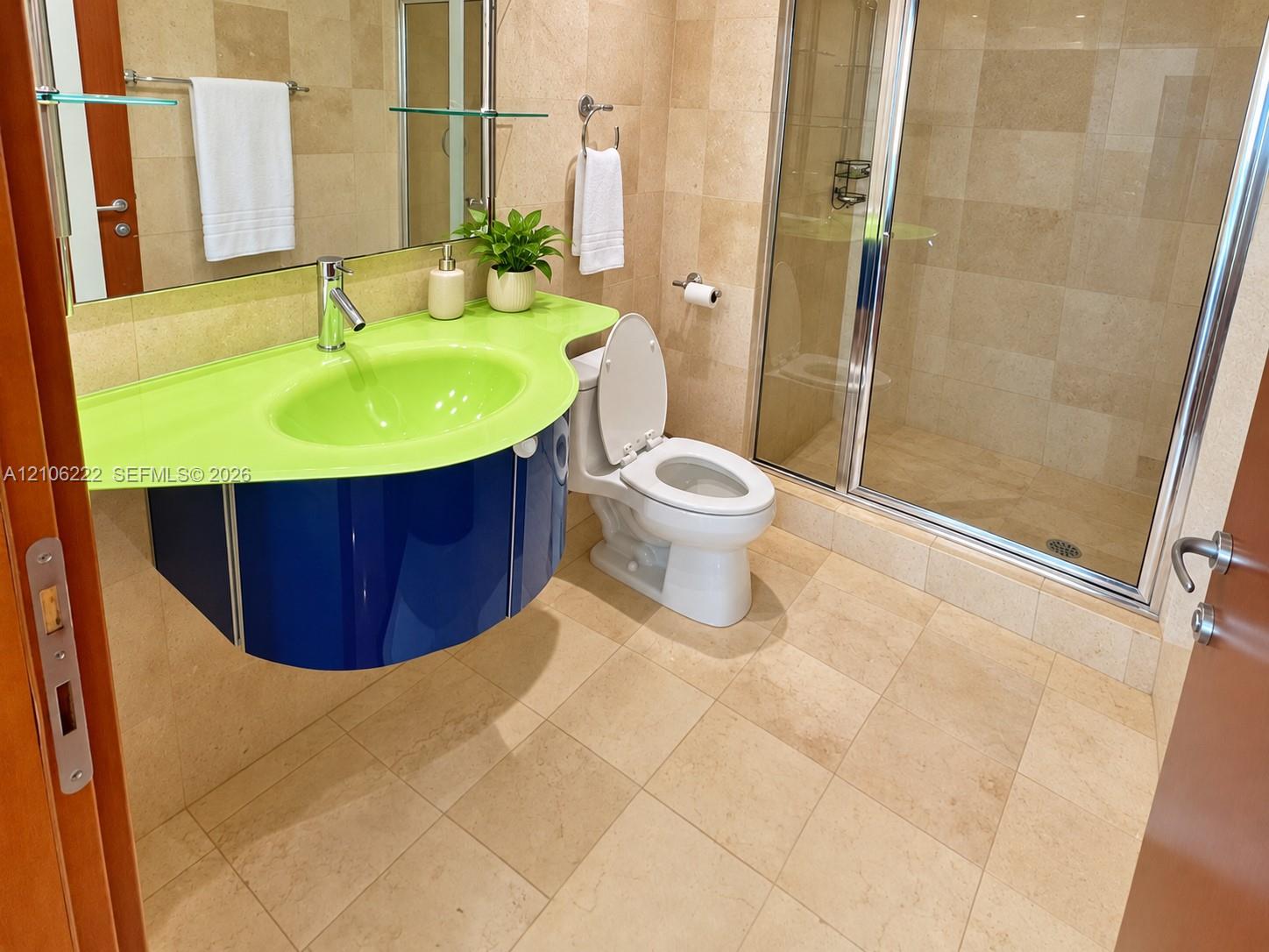 Floating vanity with a contoured countertop, wall-to-wall stone tile flooring, and walk-in shower with a glass enclosure