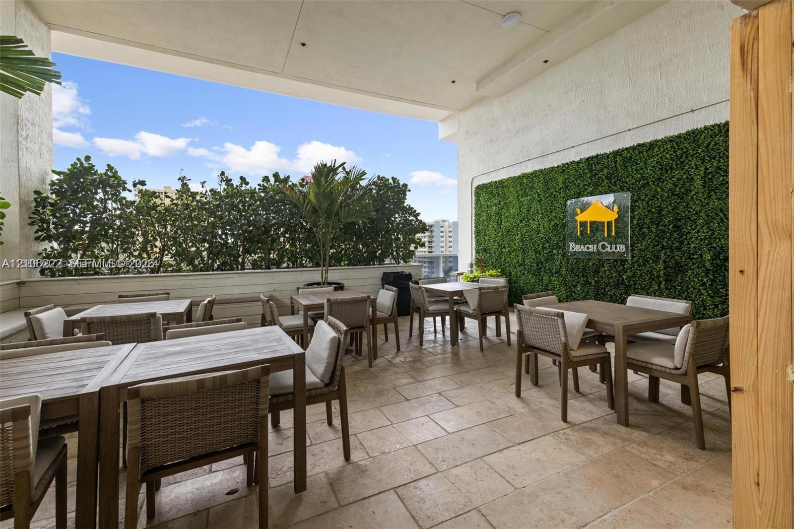 Covered outdoor terrace featuring stone tile flooring, a vertical green wall installation, recessed lighting, and perimeter shrubbery