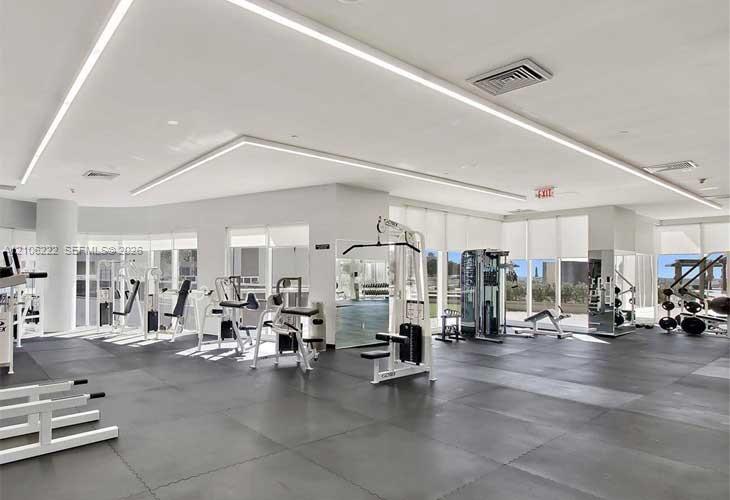 Fitness center featuring resilient rubber flooring, recessed architectural LED lighting, expansive floor-to-ceiling windows, and mirrored wall surfaces