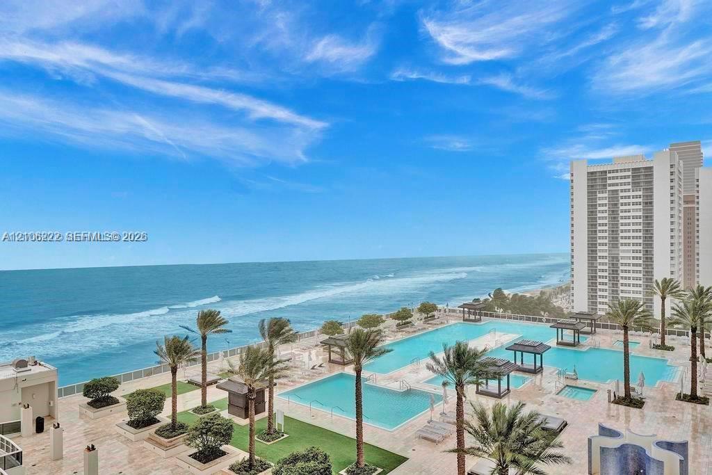 Oceanfront terrace featuring multiple swimming pools, stone-paved decking, built-in pergolas, and established palm trees