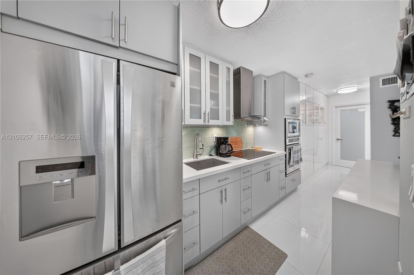 Kitchen featuring stainless steel appliances, glass-front cabinetry, integrated wall oven, solid surface countertops, and glossy tile flooring