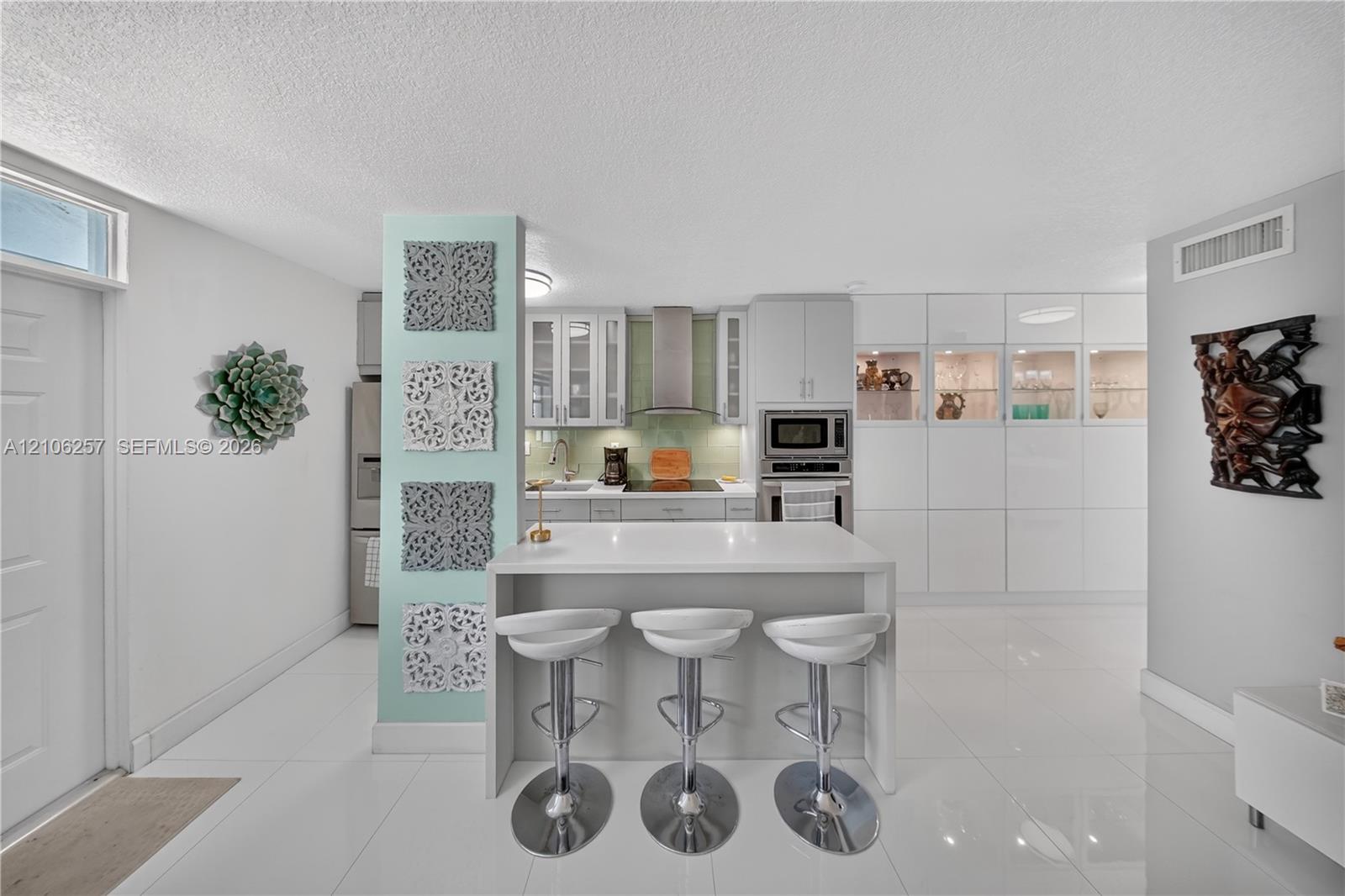 Kitchen featuring a central island with a quartz countertop, white cabinetry, integrated stainless steel appliances, a tile backsplash, and polished tile flooring. Lots of storage! Kitchen featuring a central island with a quartz countertop, white cabinetry, integrated stainless steel appliances, a tile backsplash, and polished tile flooring. Lots of storage!