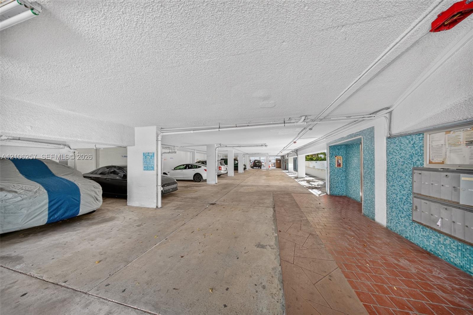 One Covered parking area featuring concrete flooring, a dedicated pedestrian walkway with brick-style pavers, and a built-in wall-mounted mailbox cluster