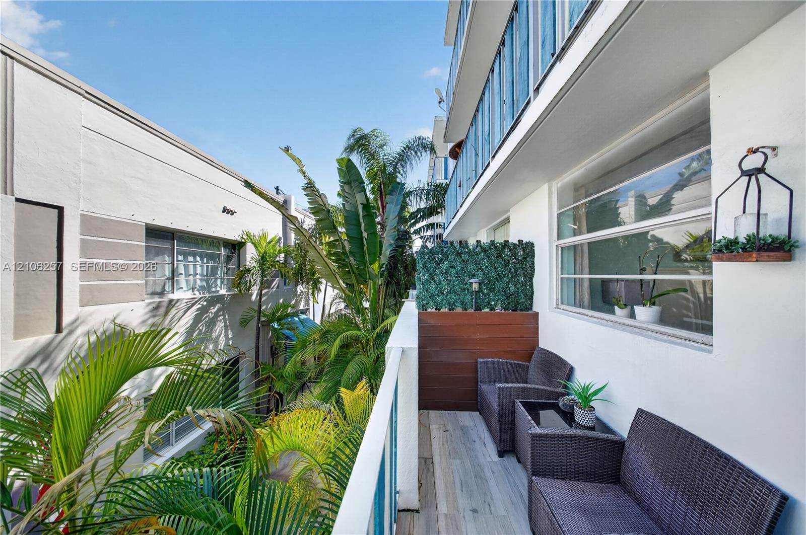 Rear Private balcony featuring wood-finish flooring, metal railing, privacy screening, and wall-mounted exterior lighting