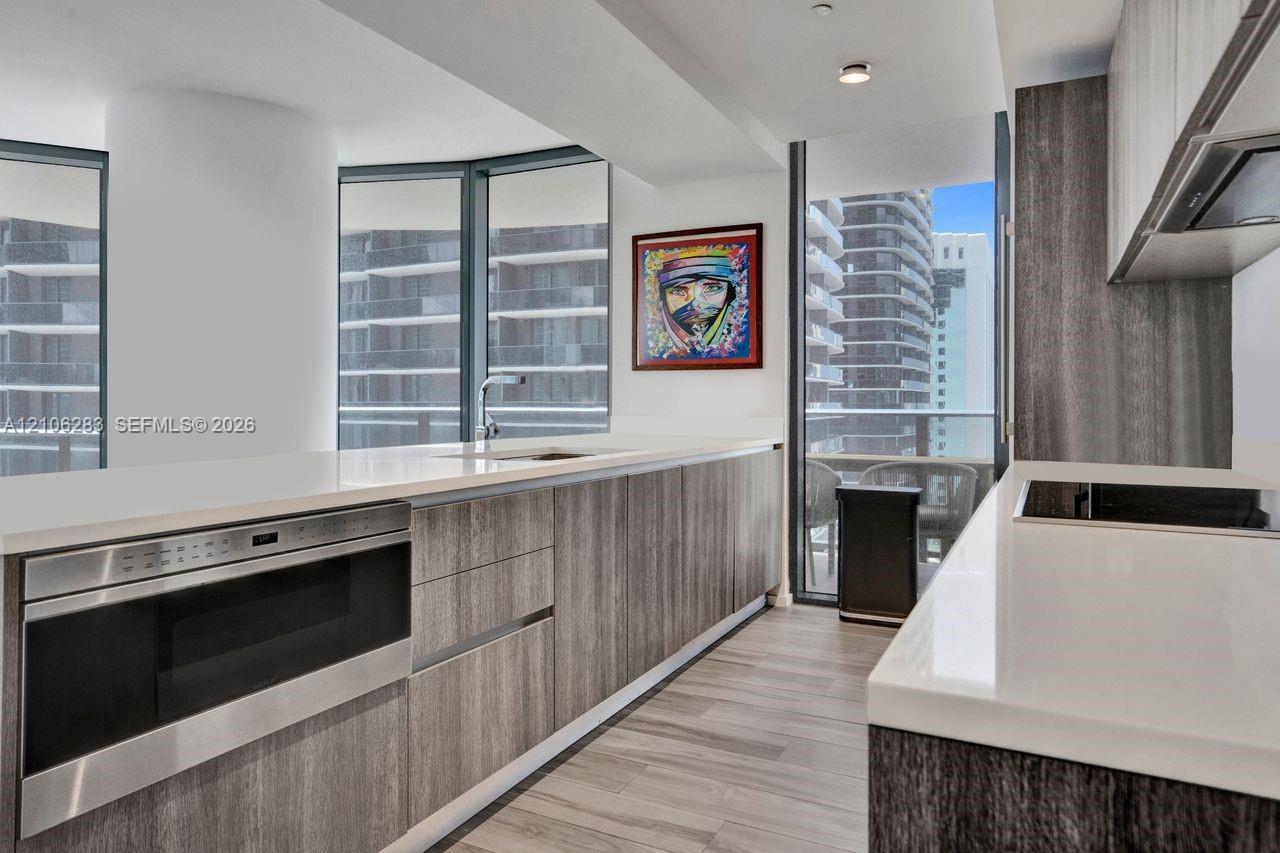 Kitchen featuring wood-finish cabinetry, stone-surface countertops, built-in stainless steel microwave, integrated stovetop, and floor-to-ceiling windows