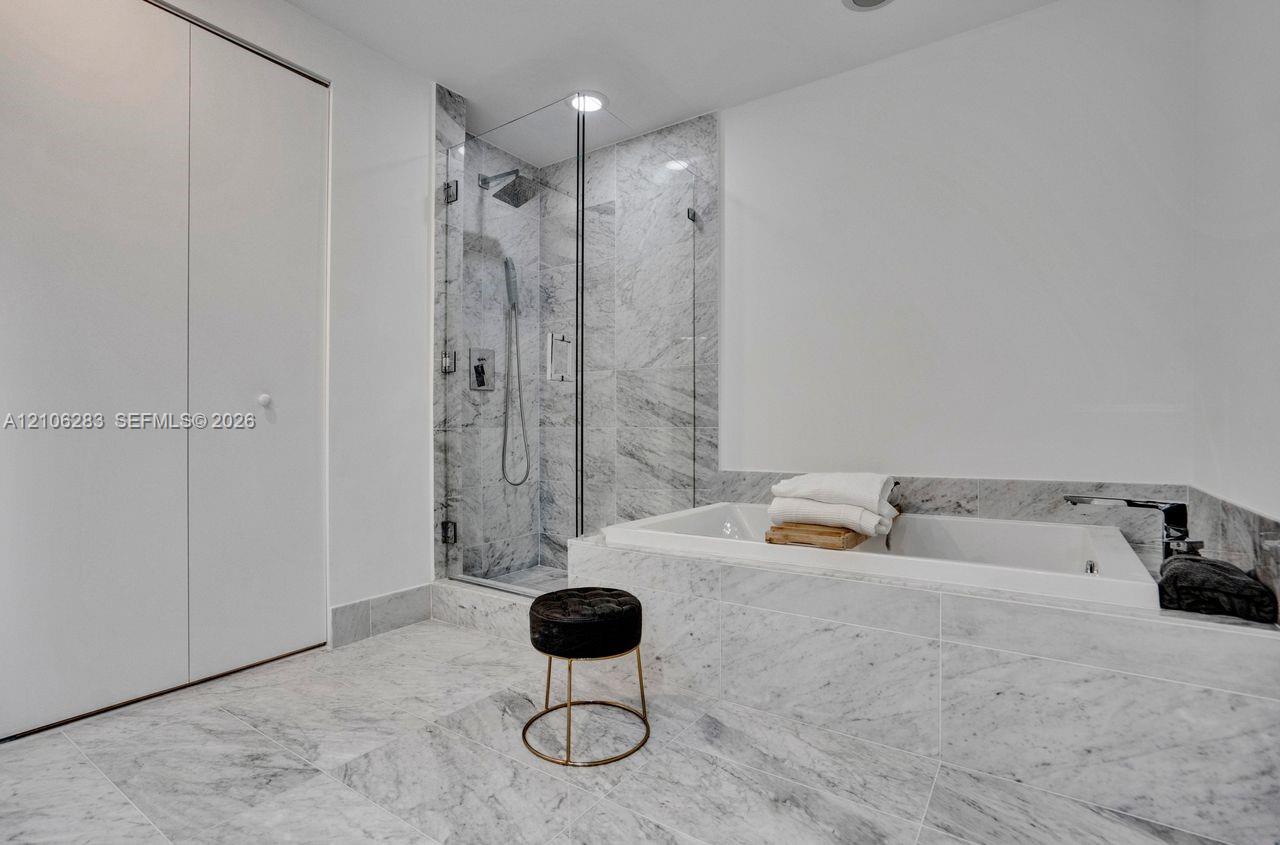 Stone-tiled bathroom featuring a walk-in shower with a glass enclosure, a deep soaking tub with stone surround, and recessed lighting