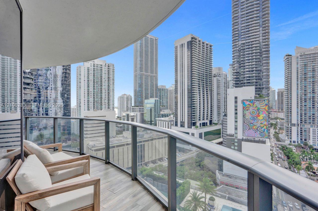 Private balcony with tile flooring and a glass-paneled railing overlooking an urban cityscape