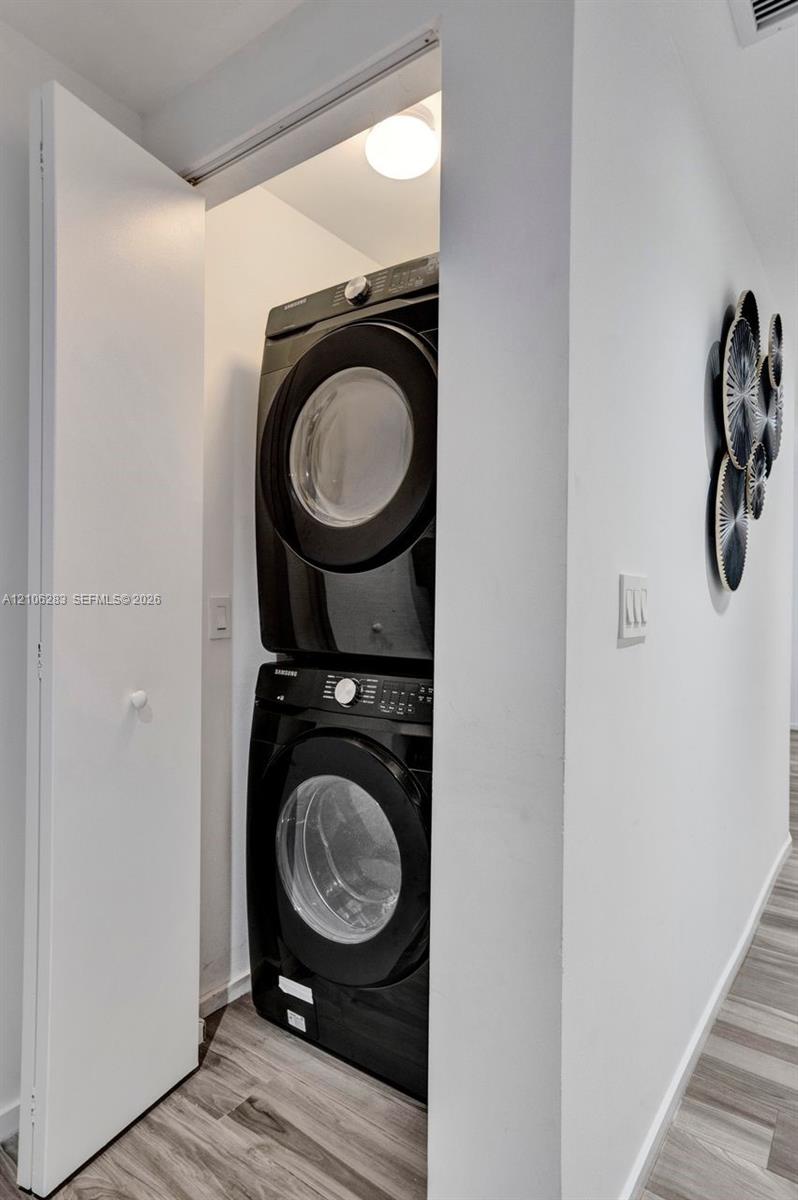Laundry closet featuring stackable appliances and wood-finish flooring