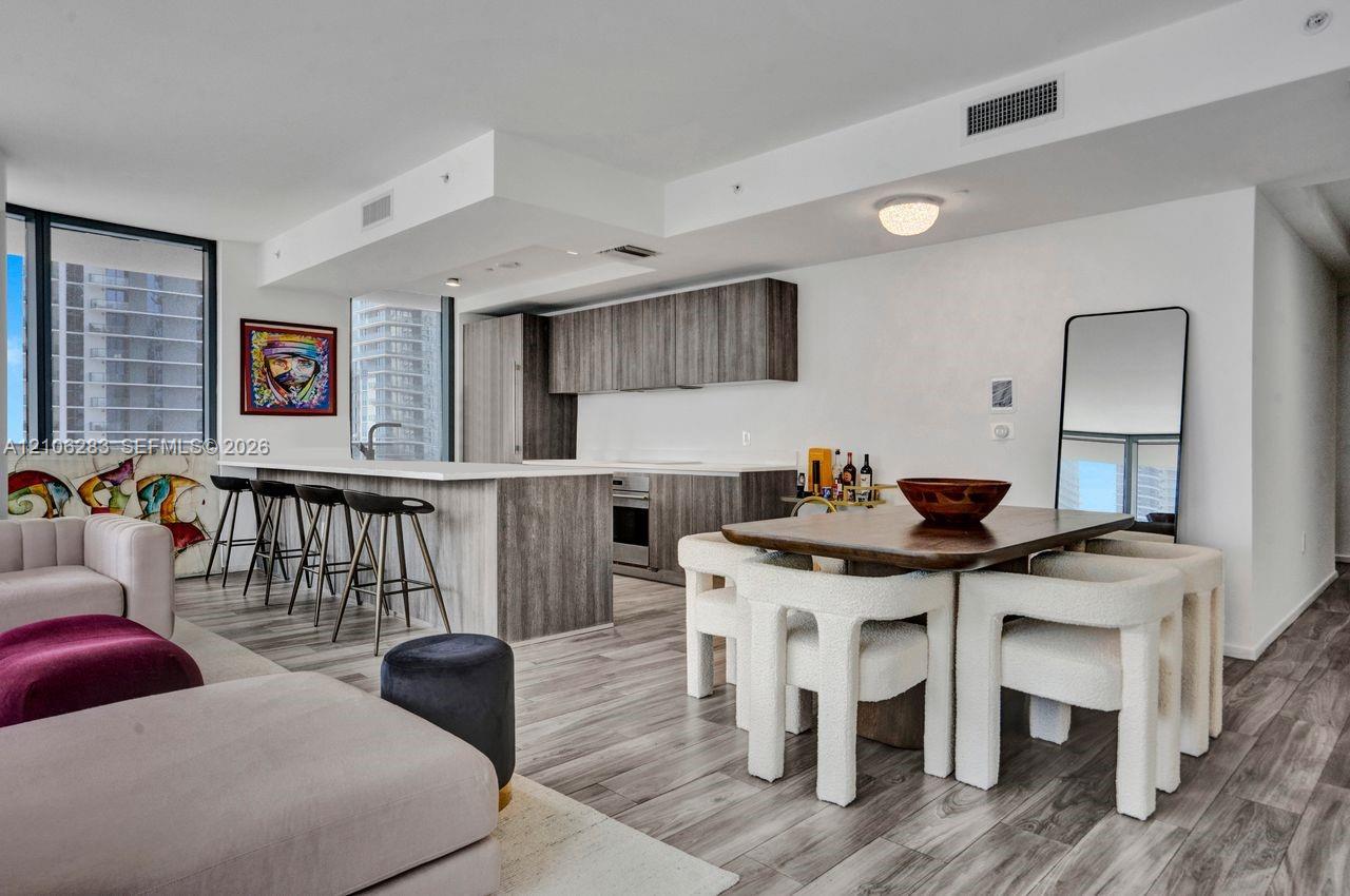 Open-concept kitchen featuring flat-panel wood-finish cabinetry, a large kitchen island with countertop seating, stainless steel appliances, and wood-finish flooring throughout