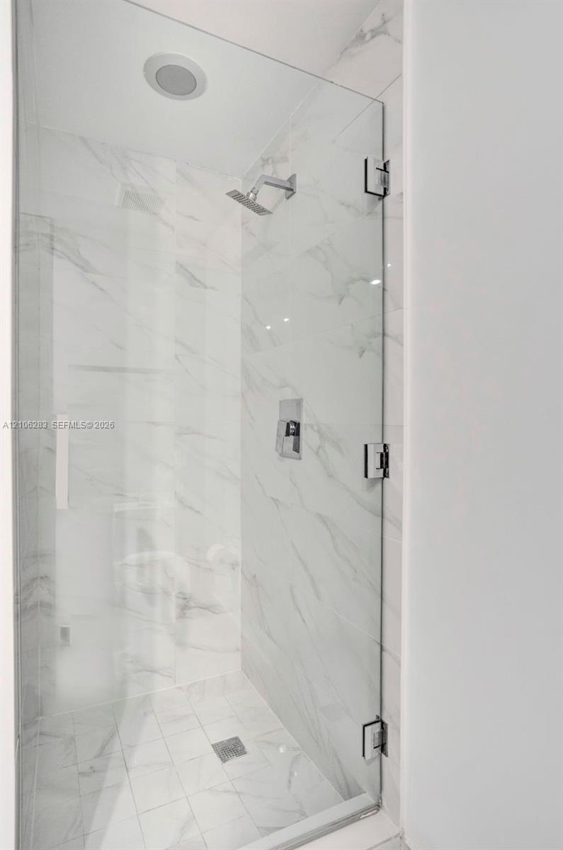 Walk-in shower featuring a frameless glass door, wall-to-wall stone-finish tile, recessed ceiling light, and polished chrome fixtures