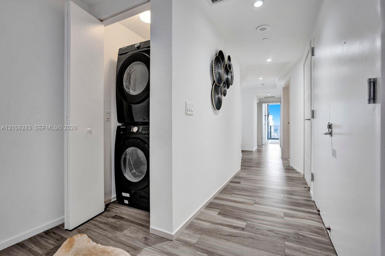 Stacked laundry unit housed within a dedicated closet, featuring wood-finish flooring and recessed ceiling lighting