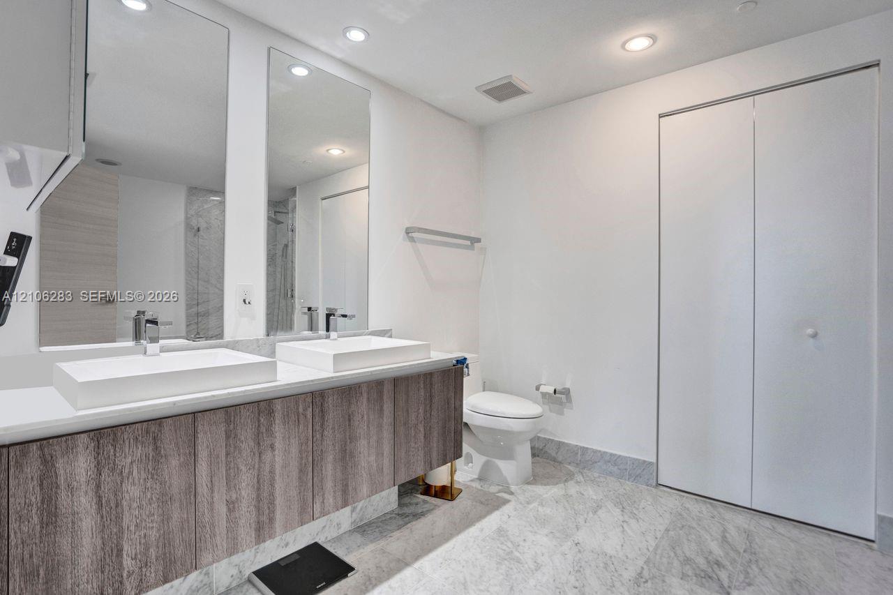 Floating vanity with dual rectangular vessel sinks, stone-finish flooring, full-height wall mirrors, and bifold closet doors