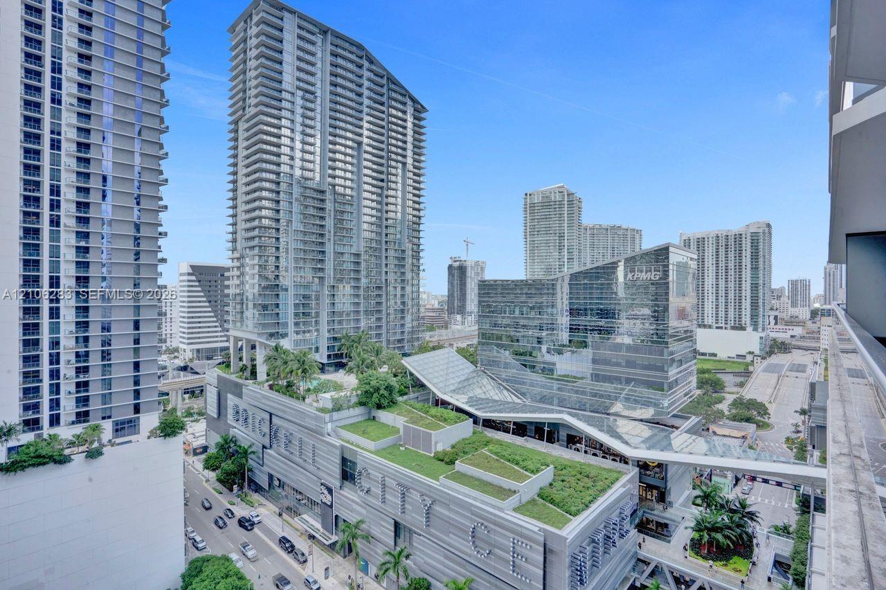 Elevated balcony featuring a glass panel railing, showcasing an expansive cityscape, high-rise architectural surroundings, and integrated green roof structures