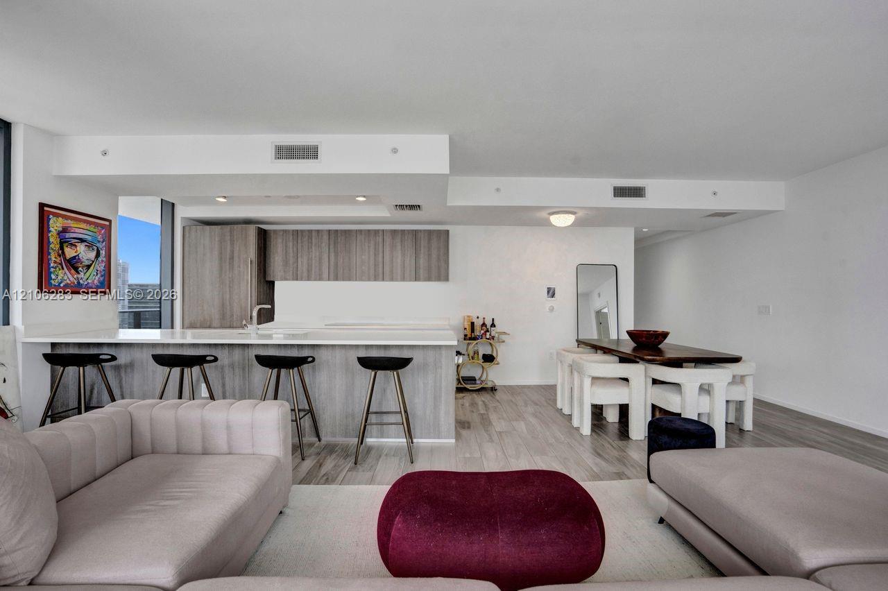 Open-concept living space featuring wood-finish flooring, a kitchen island with stone countertop, and contemporary flat-panel cabinetry