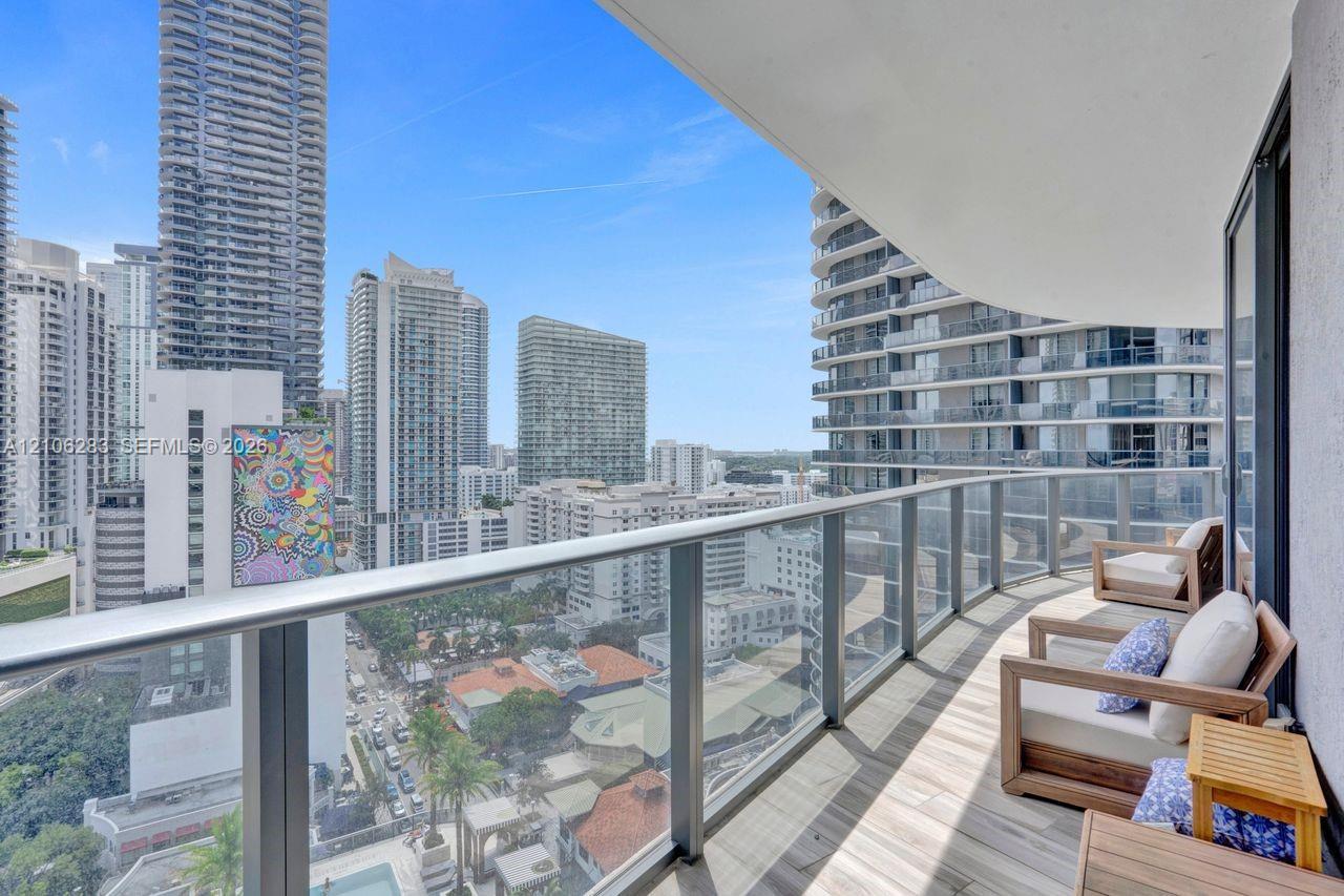 Covered balcony featuring wood-finish flooring, glass-panel railing, and a metal handrail