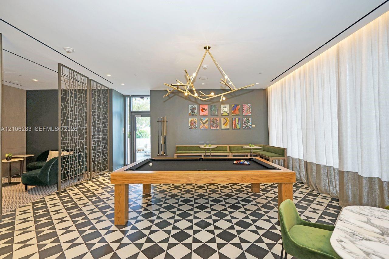 Geometric patterned tile flooring, decorative metal room divider, branching sculptural pendant light, recessed ceiling lighting, and floor-to-ceiling drapery