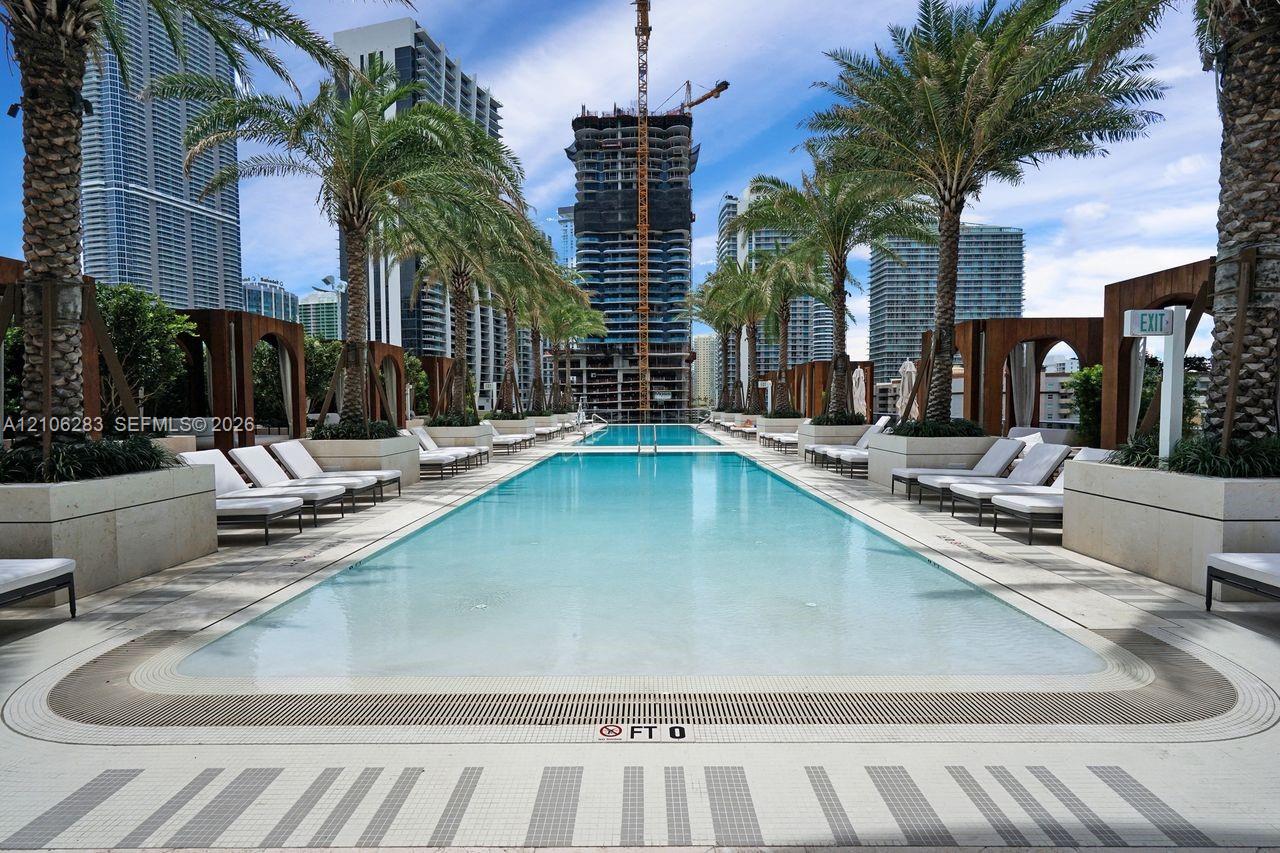 Rectangular swimming pool featuring stone-tile decking, built-in wooden cabanas, mature palm trees, and integrated landscaping planters