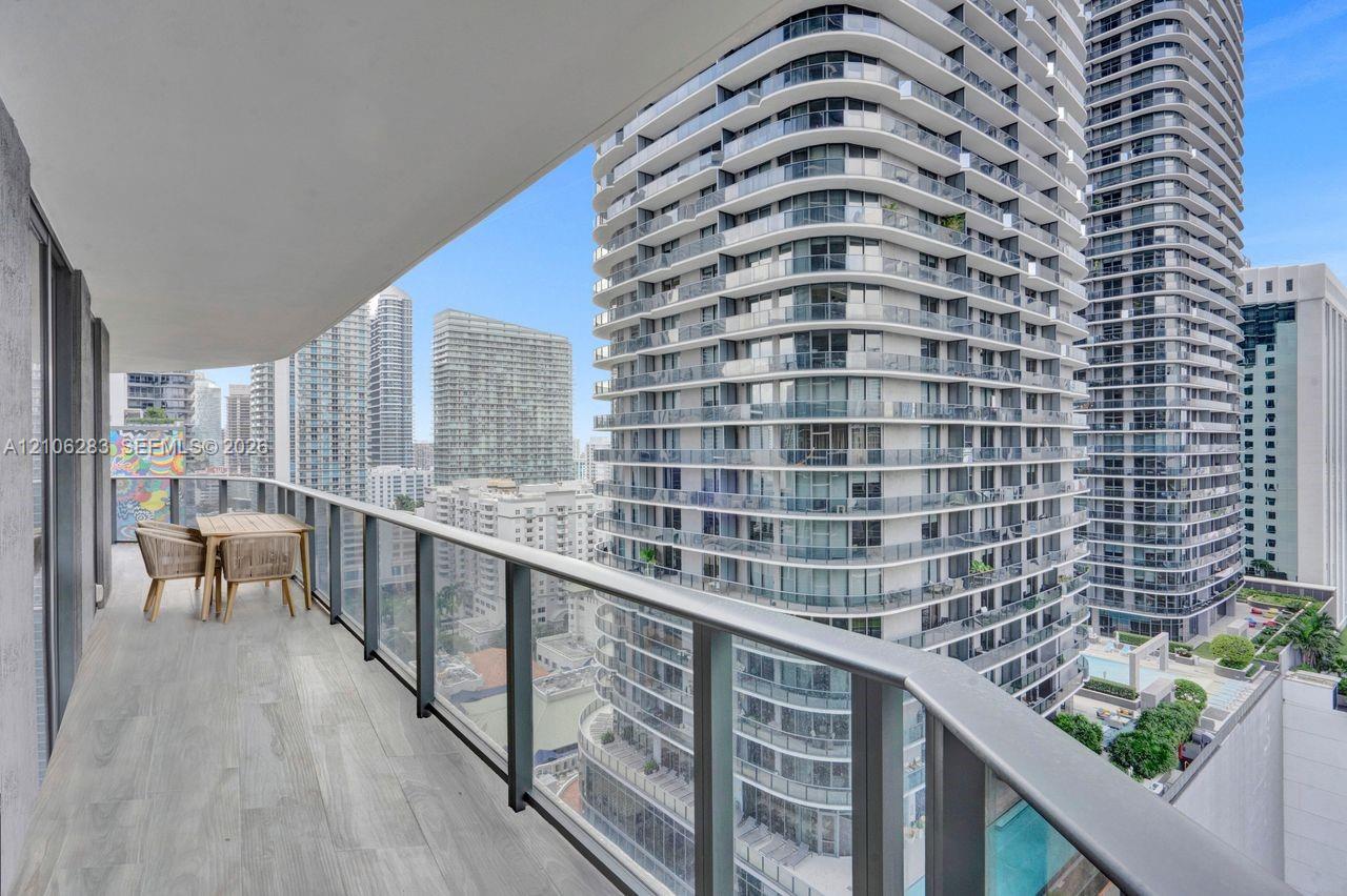 Covered balcony featuring wood-finish flooring and a glass-paneled railing with a metal handrail