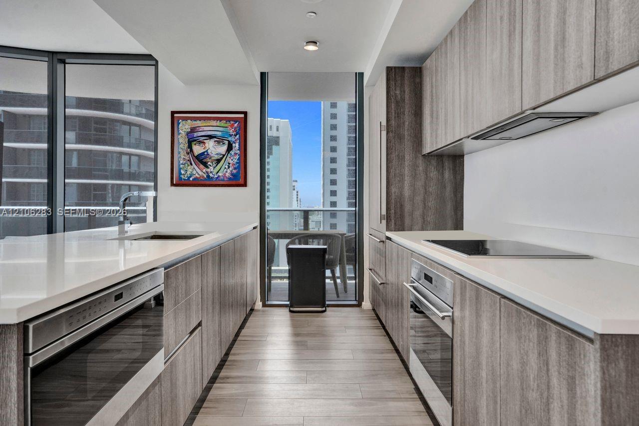 Galley kitchen featuring wood-finish cabinetry, quartz countertops, integrated stainless steel appliances, and wood-finish flooring