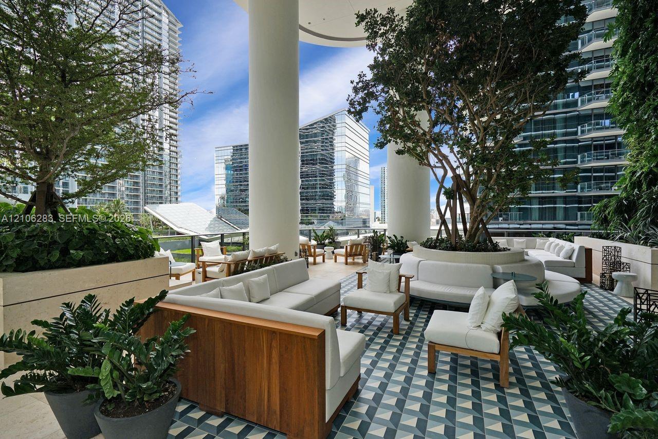 Covered outdoor terrace featuring geometric patterned tile flooring, structural concrete pillars, and integrated stone planters with mature landscaping
