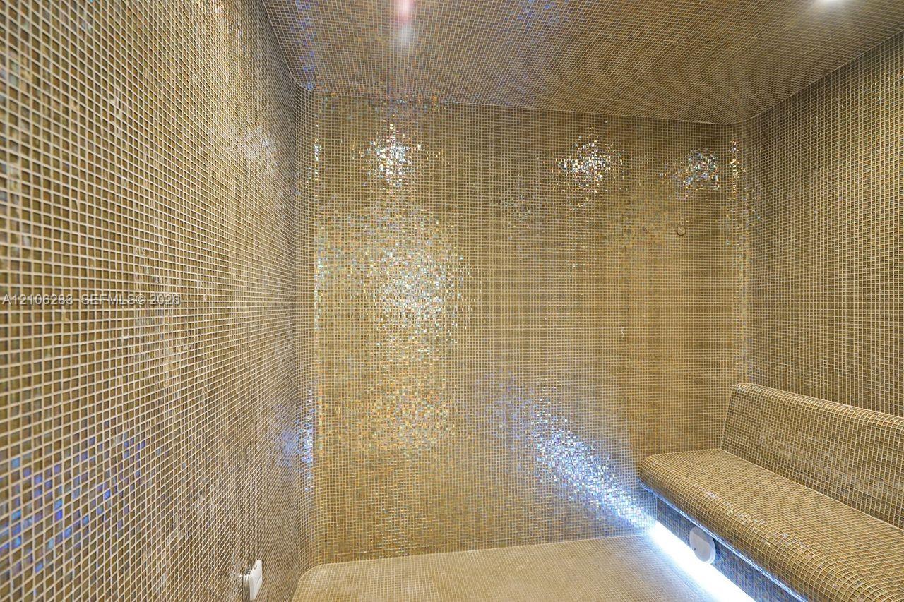 Enclosed steam room featuring floor-to-ceiling metallic mosaic tile, built-in tiled bench, and integrated LED accent lighting