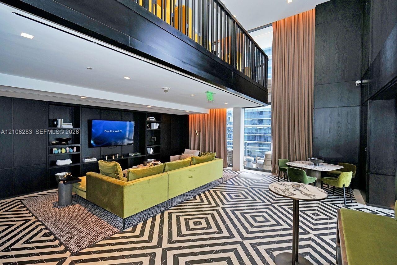 Double-height living area featuring floor-to-ceiling windows, built-in floor-to-ceiling cabinetry, a mezzanine level with black metal railing, and patterned geometric floor tile