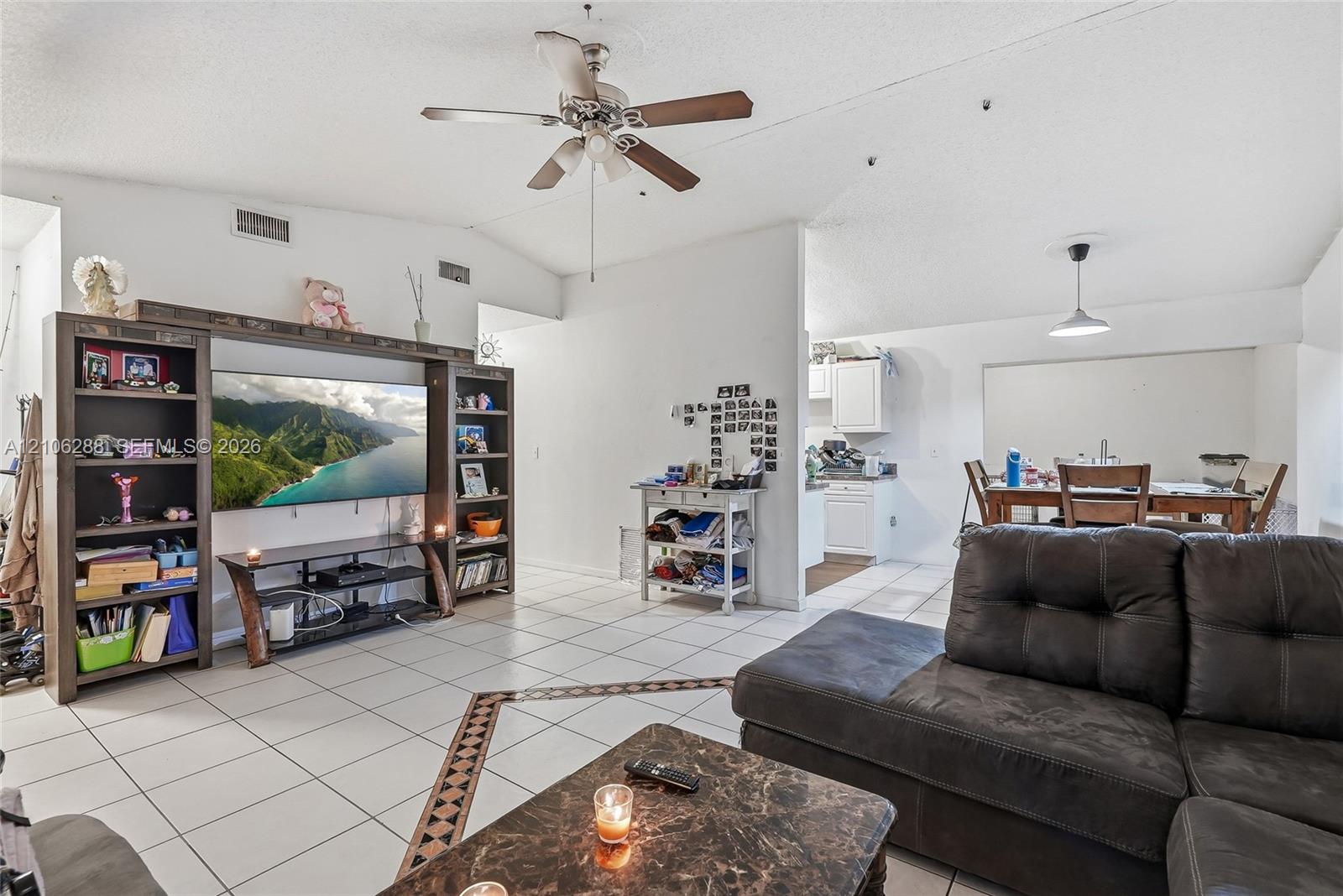 Open-concept interior featuring vaulted ceilings, oversized white floor tile with decorative border inlay, and a built-in media center with integrated shelving