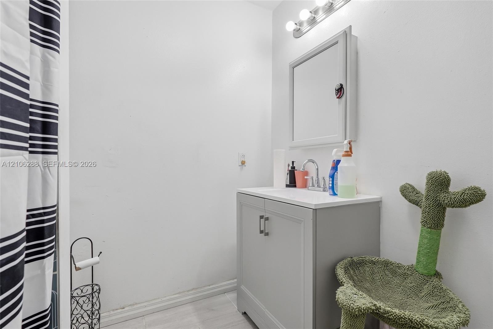 Bathroom vanity featuring a solid-surface countertop, dual-door gray cabinet, and wall-mounted medicine cabinet with a three-light fixture