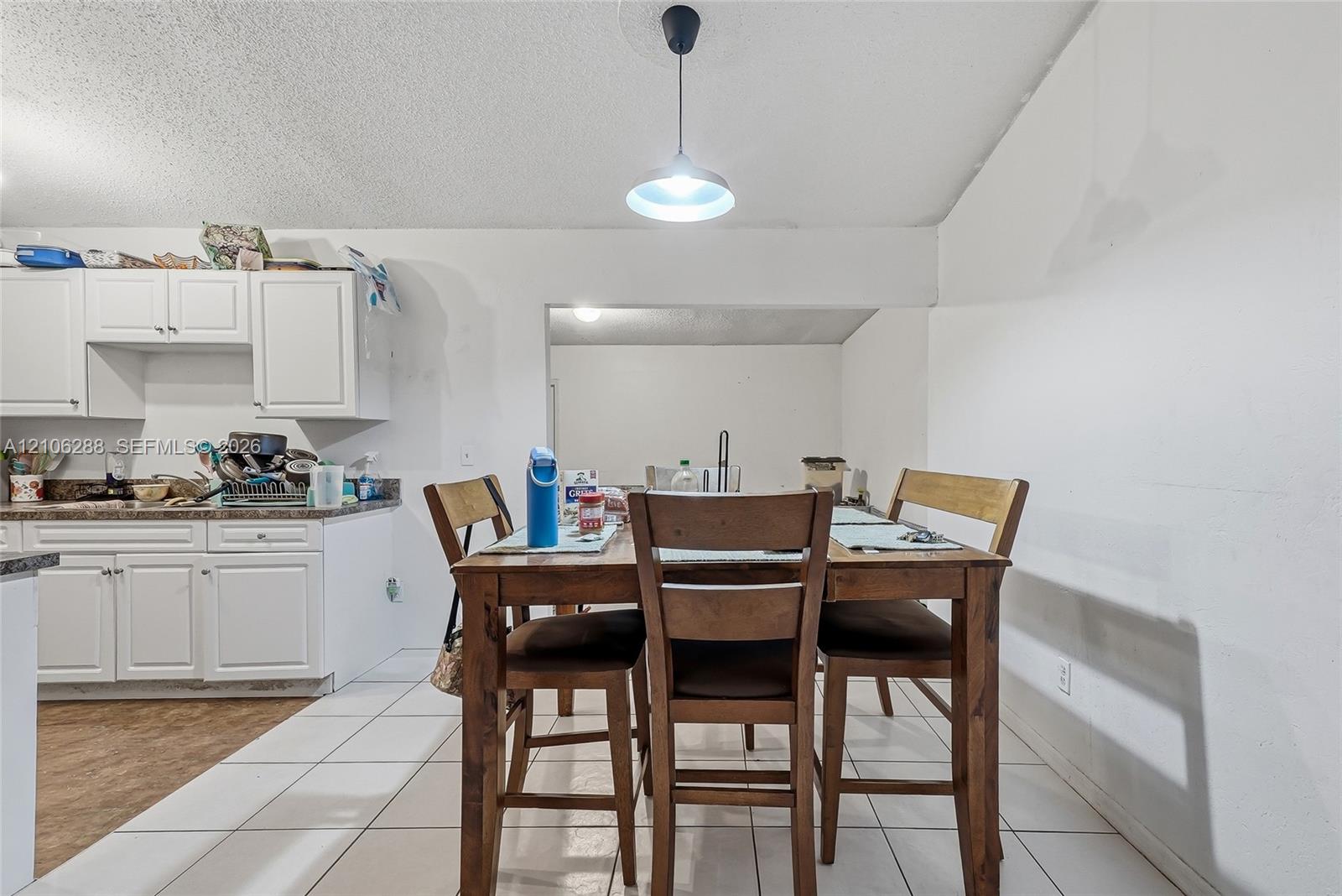 White cabinetry with coordinating countertops, tile flooring, and a pendant light fixture