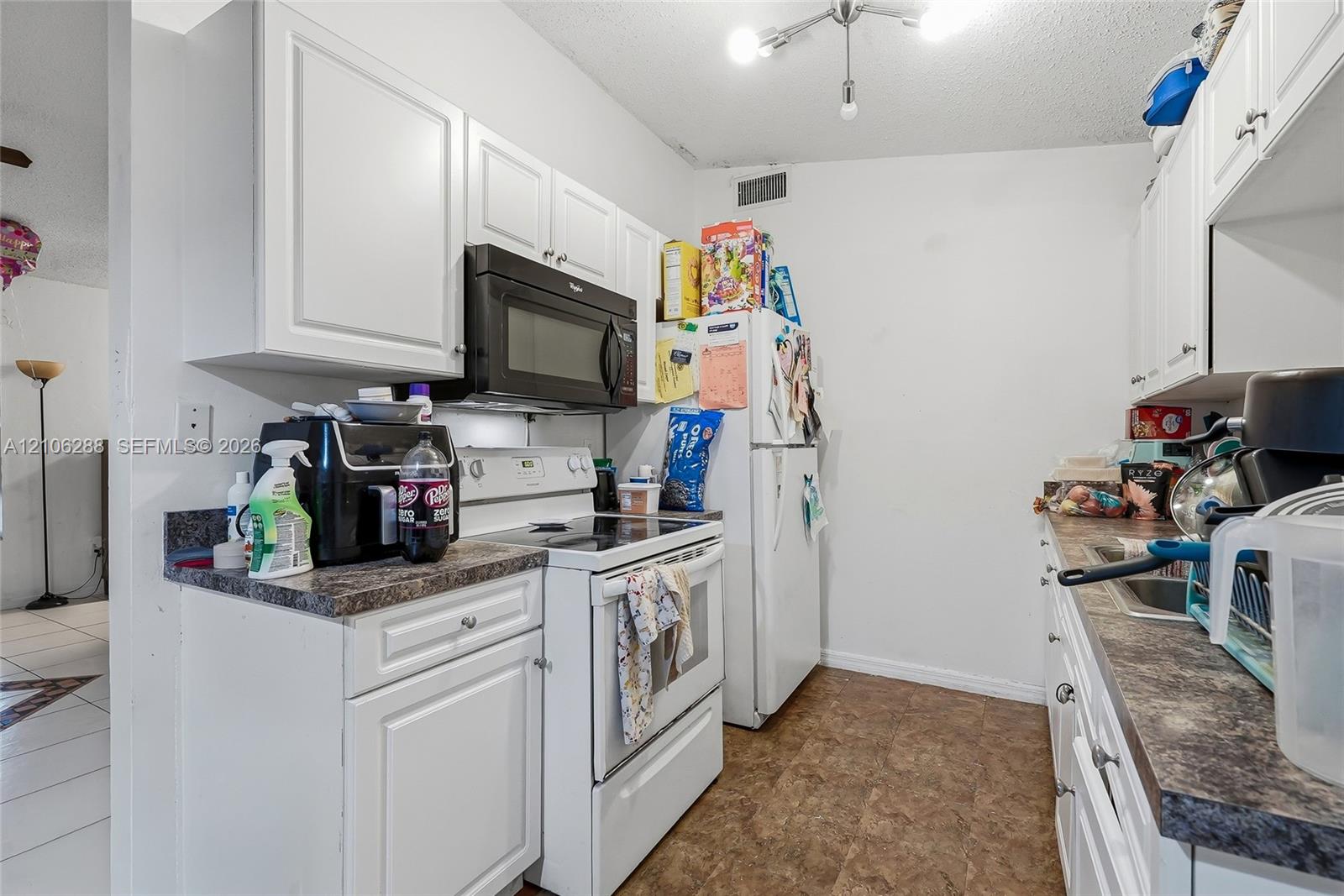 Kitchen featuring white cabinetry, dark stone-finish countertops, over-the-range microwave, white appliances, and tiled flooring