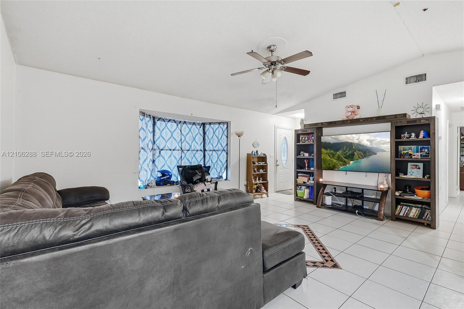Living area featuring a vaulted ceiling, tile flooring, bay window, and a built-in media center with shelving