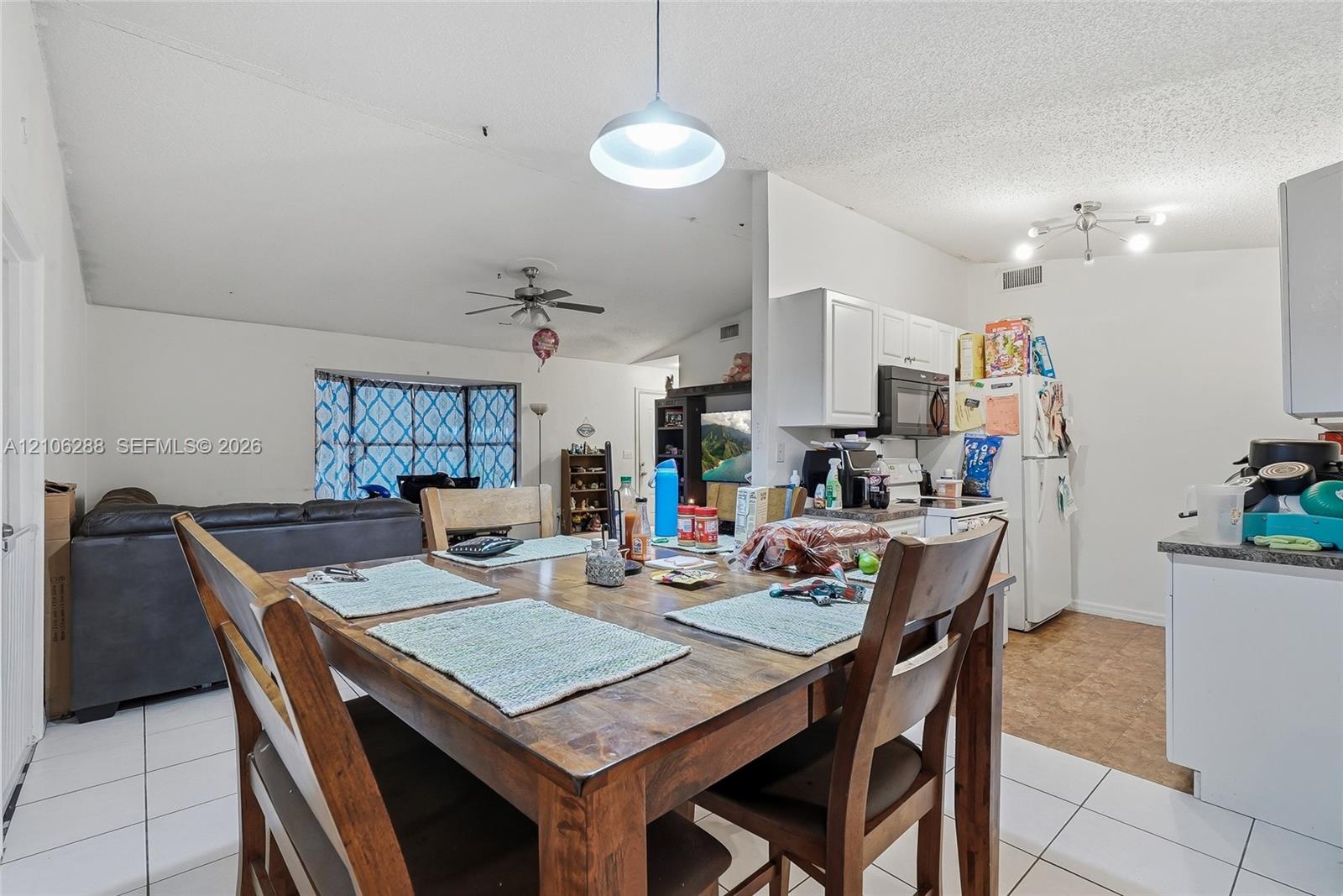 Vaulted ceilings, kitchen featuring white cabinetry, pendant lighting, ceiling fan, and bay window