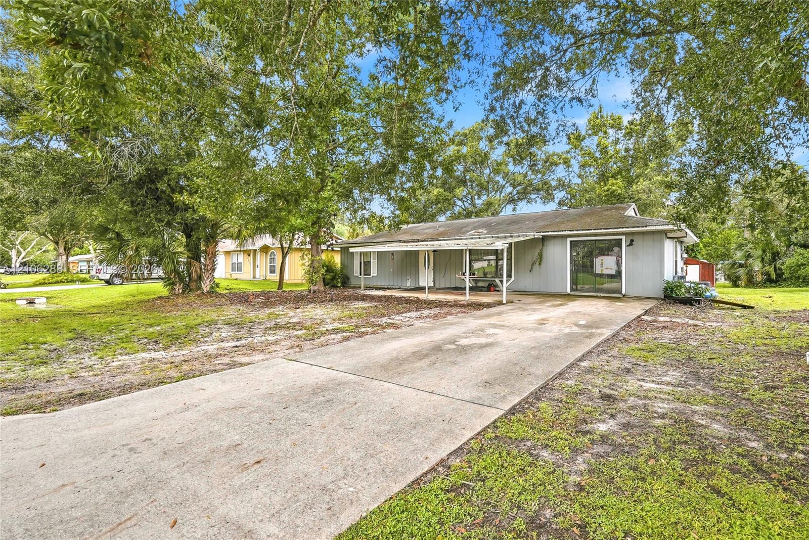 Single-story exterior featuring gray siding, a covered front porch, and a concrete driveway shaded by mature trees