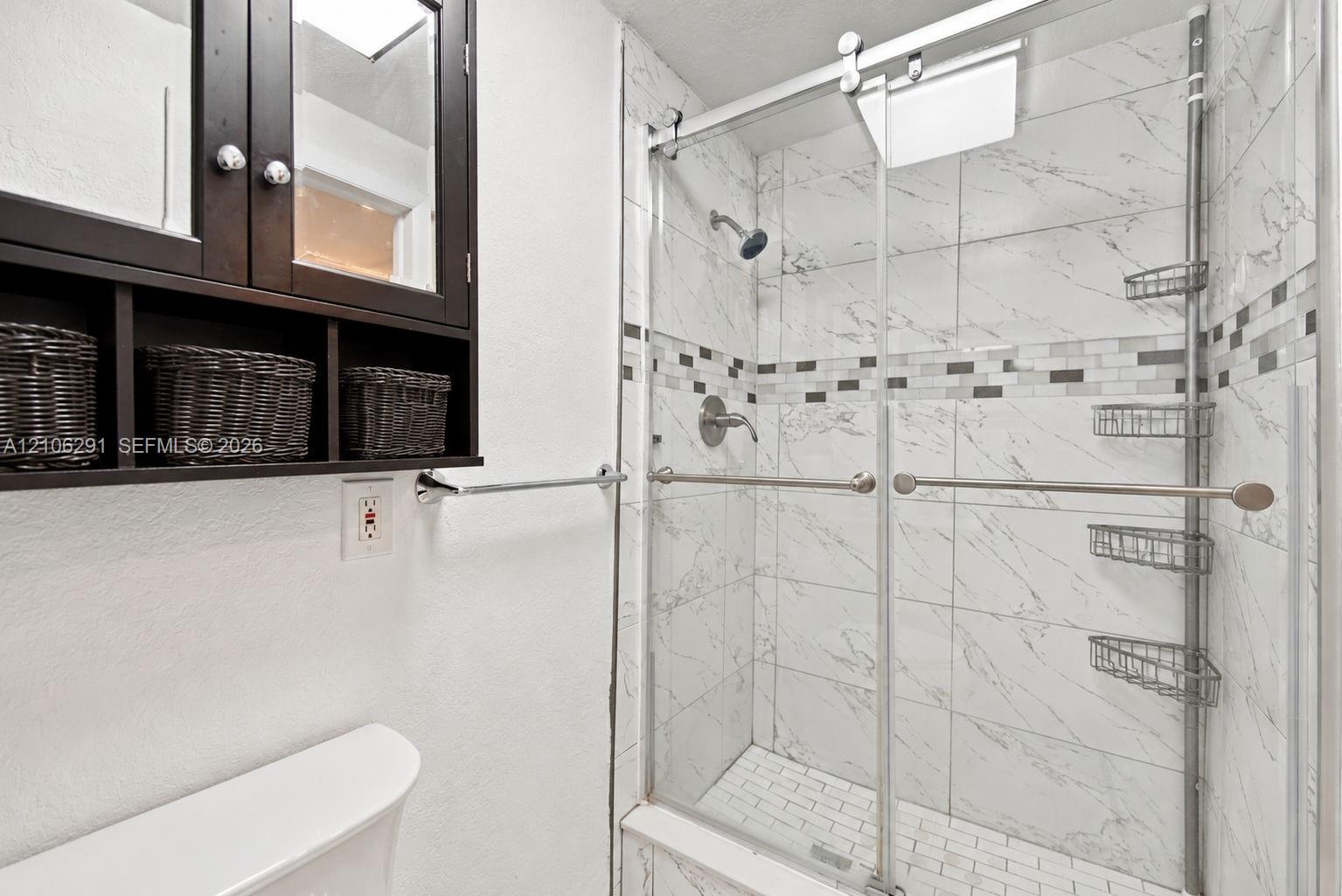 Walk-in shower featuring large-format stone-patterned tile walls, a linear mosaic accent border, a glass sliding door, and a subway-tile patterned floor