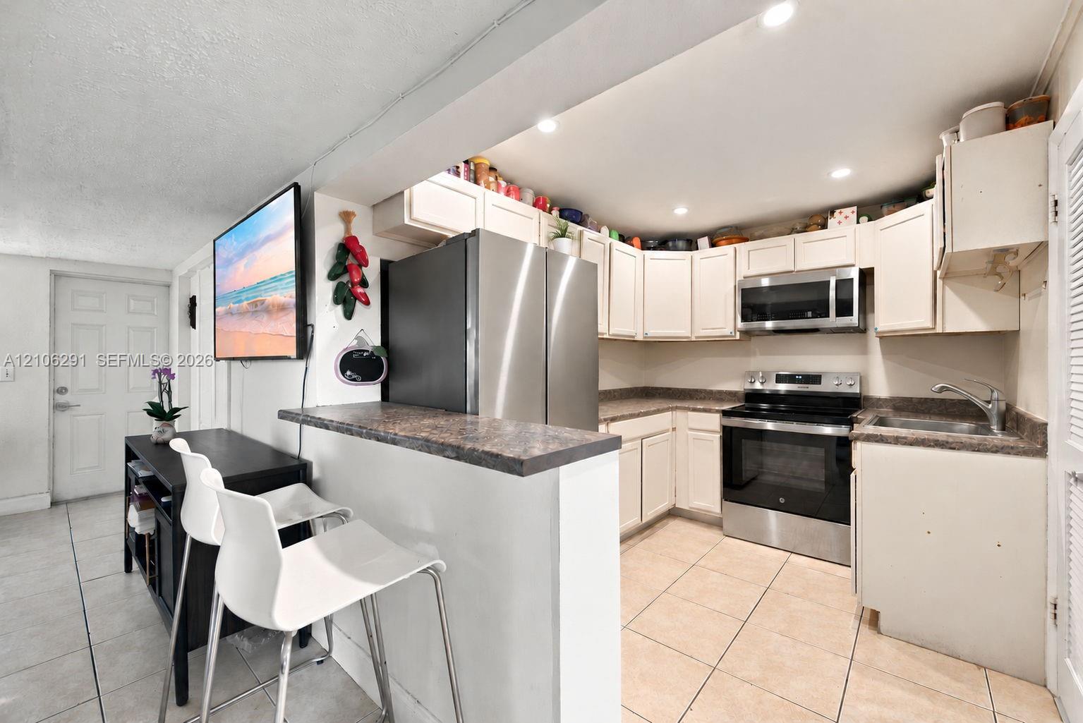 Kitchen featuring stainless steel appliances, white cabinetry, a breakfast bar with stone-finish countertop, and tile flooring