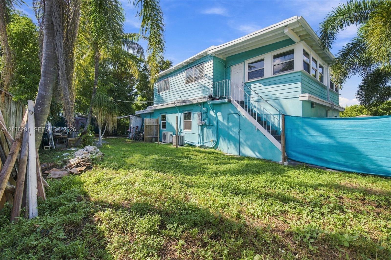 Two-story residence featuring horizontal lap siding, an exterior staircase with metal railing, and a private yard with mature palm trees