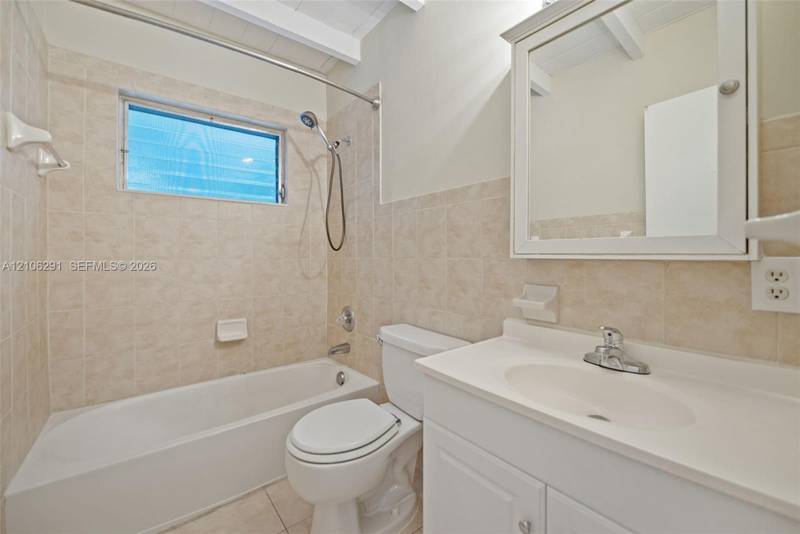 Bathroom featuring tile tub surround, integrated vanity sink, mirrored medicine cabinet, exposed wood-beam ceiling, and porcelain tile flooring