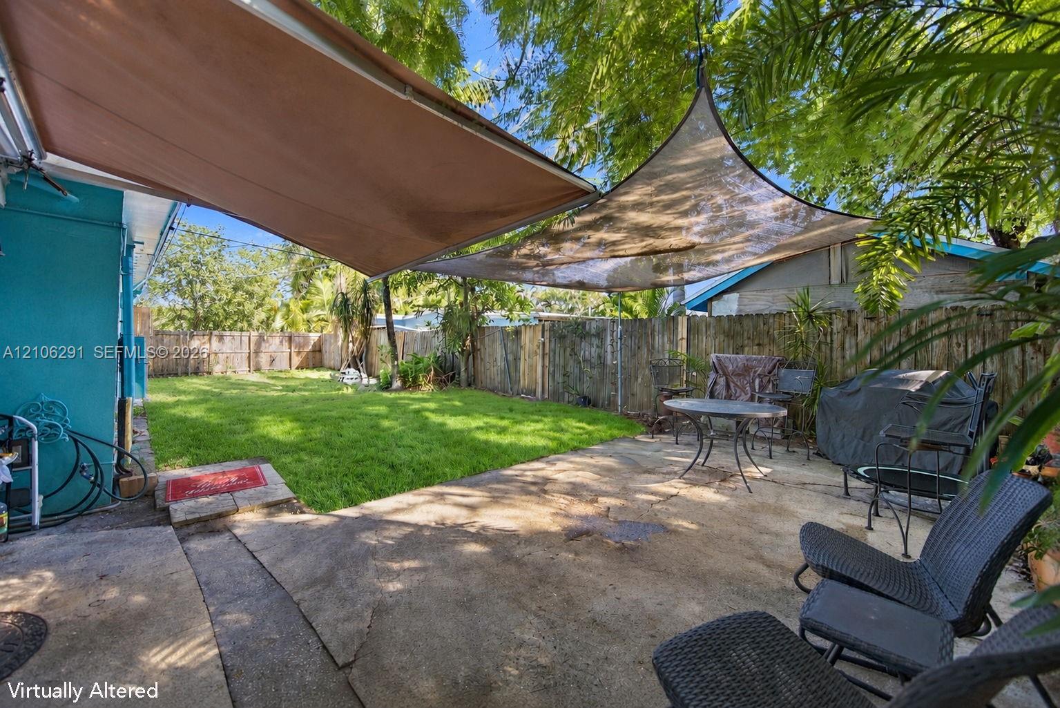 Backyard featuring a concrete patio, overhead fabric shade structure, green lawn, and perimeter wood fencing