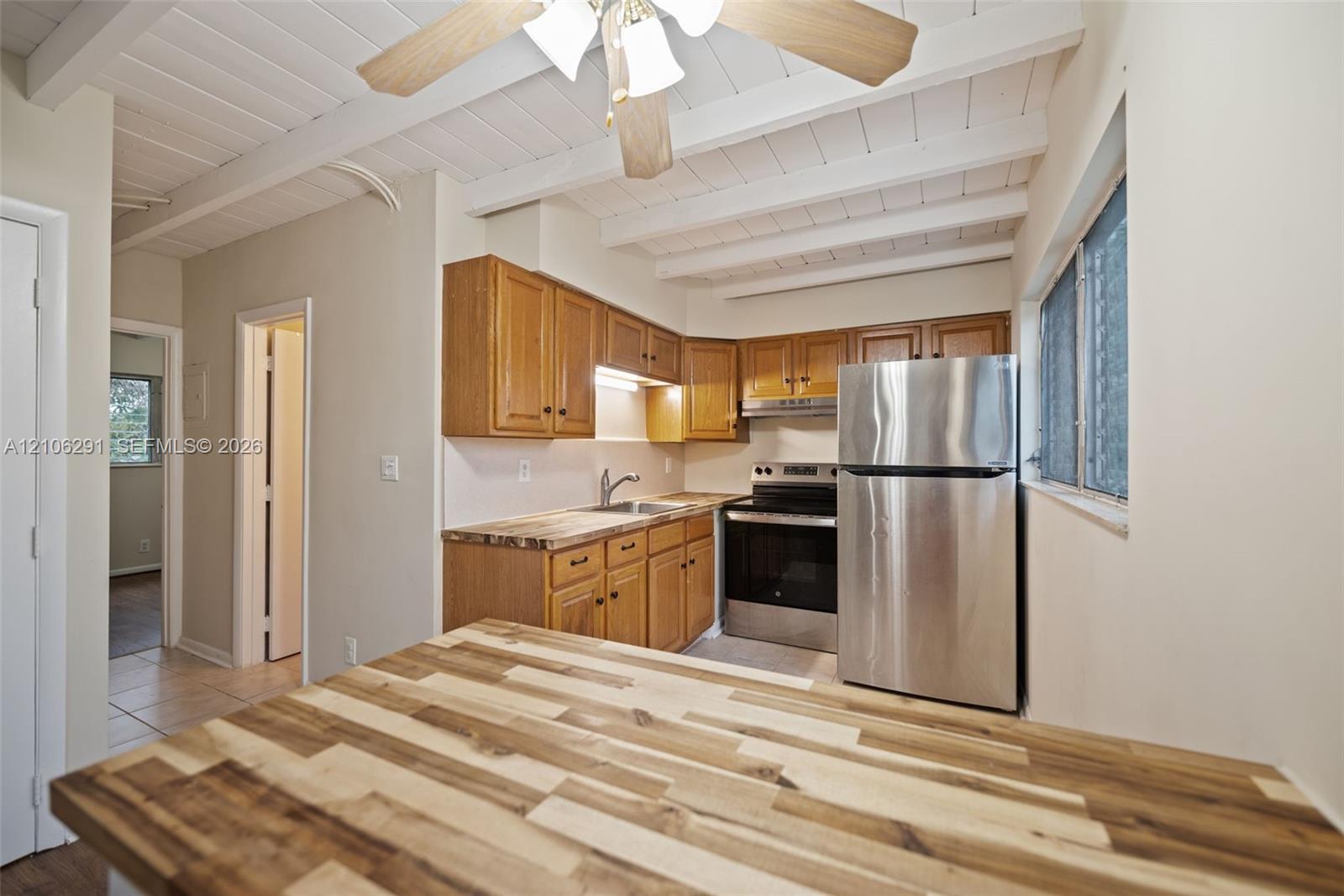 Kitchen featuring wood cabinetry, stainless steel appliances, a wood-surface island, and exposed beam ceilings