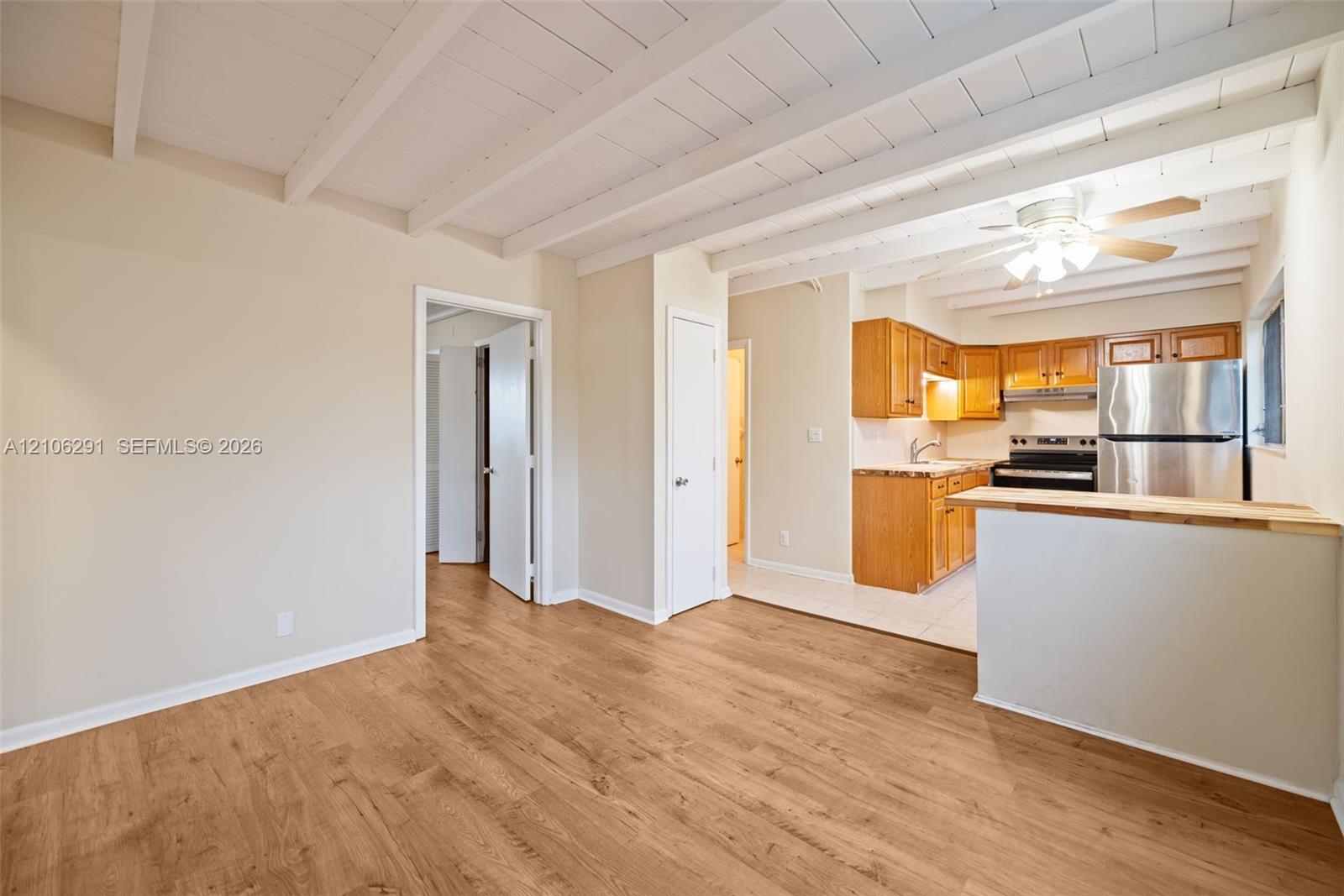 Exposed beam ceiling featuring white-painted finish, wood-finish flooring, and kitchen area with natural wood cabinetry, stainless steel refrigerator, and peninsula