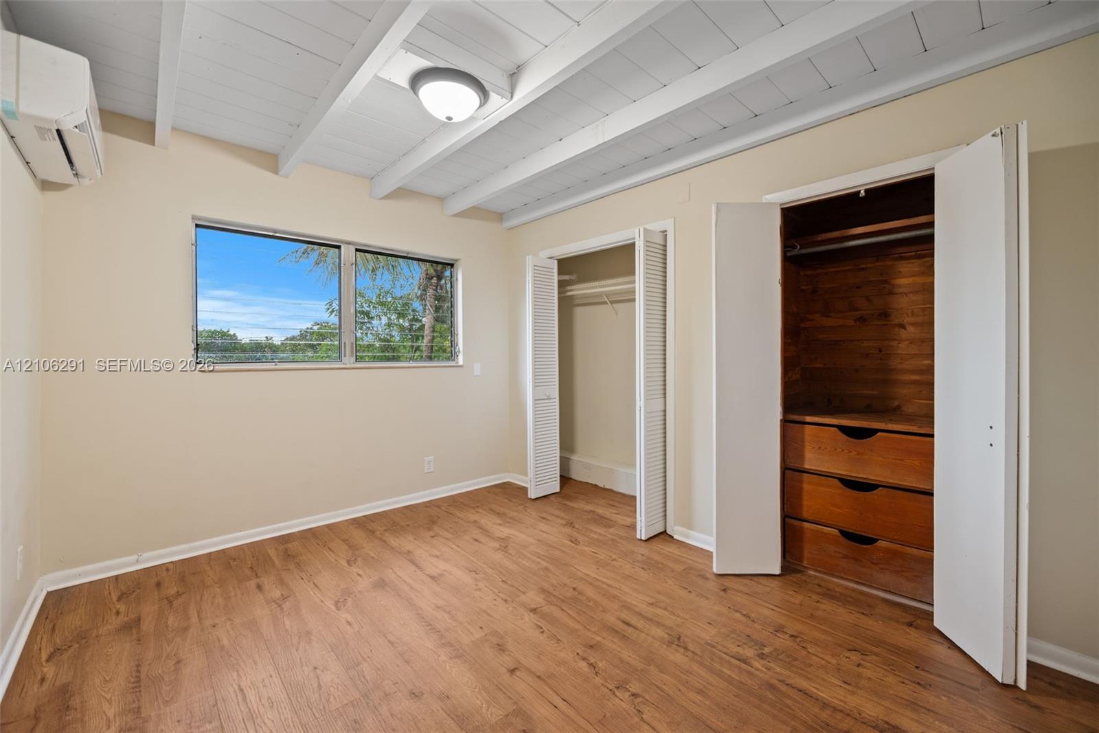 Room featuring a vaulted ceiling with exposed painted beams, wood-finish flooring, a horizontal sliding window, and built-in closet cabinetry with integrated shelving and drawers