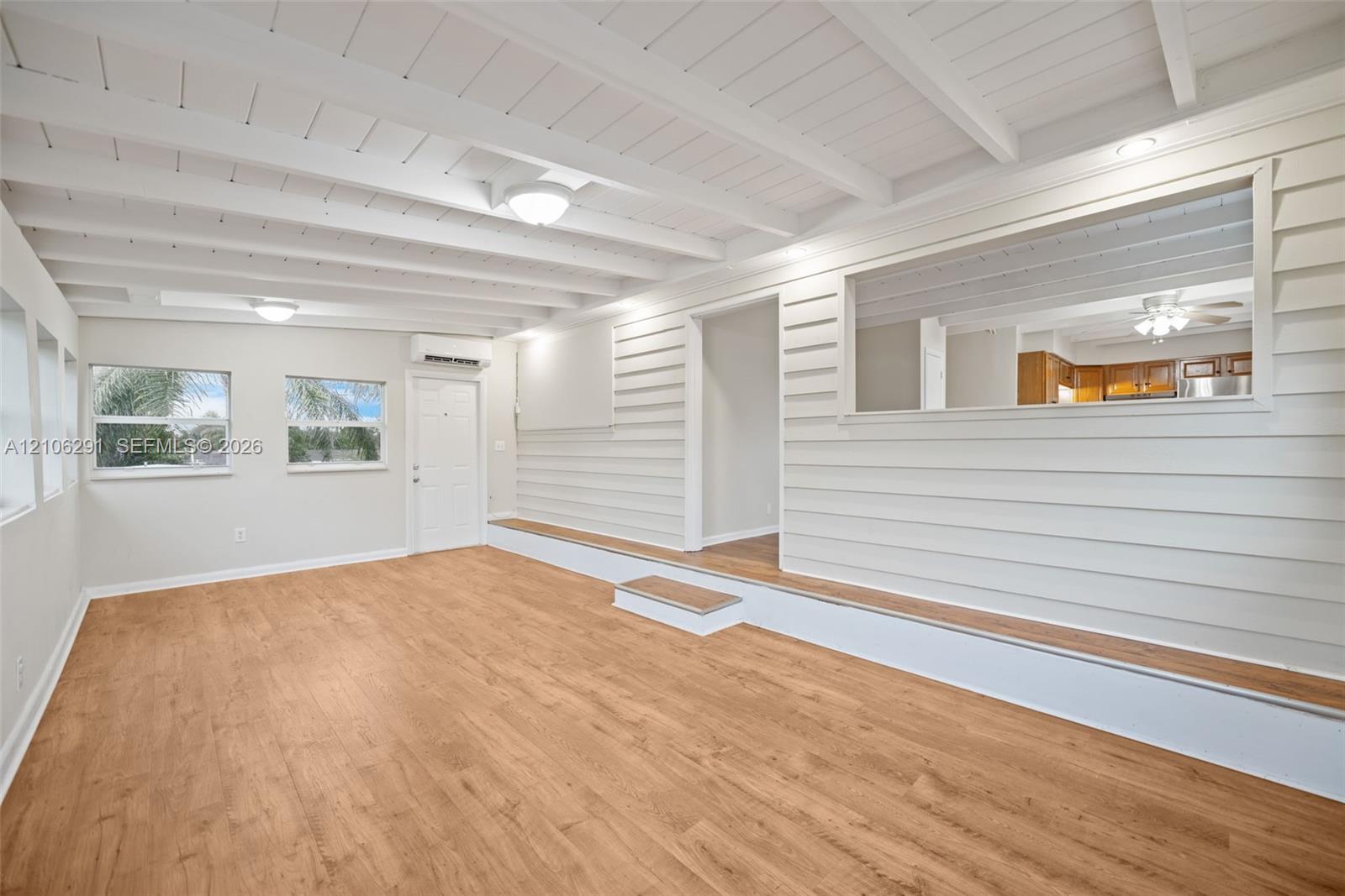 Interior featuring exposed beam ceilings, wood-finish flooring, horizontal shiplap wall paneling, a tiered floor elevation, and a rectangular pass-through opening