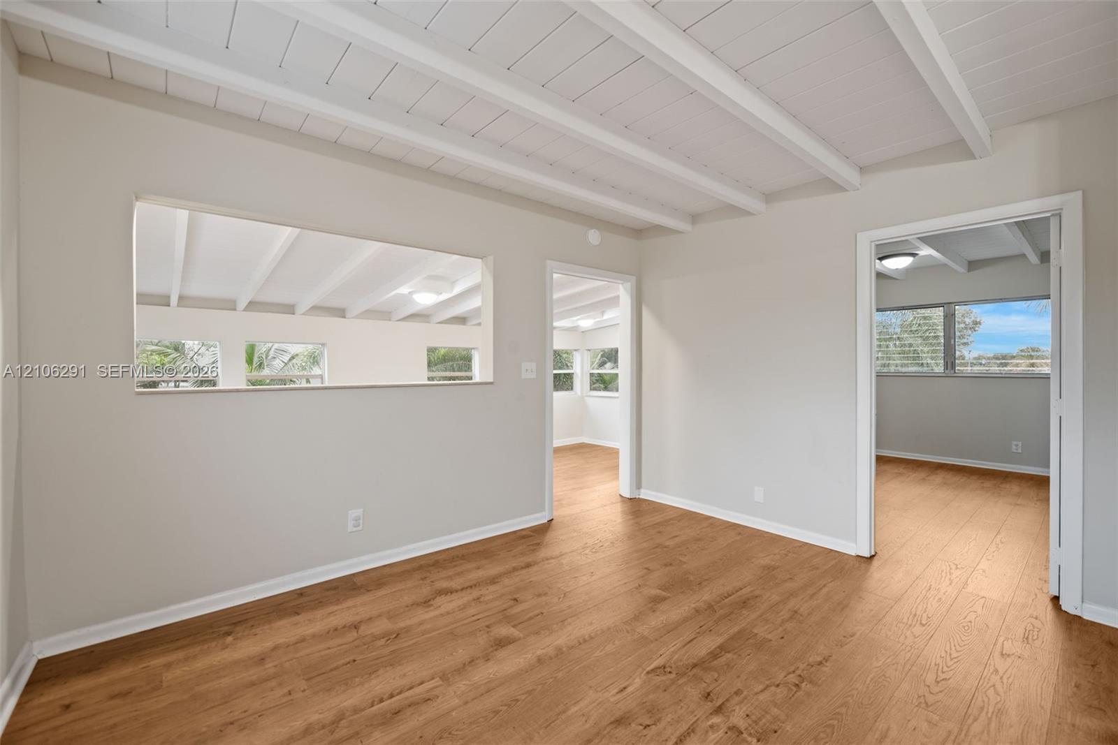 Wood-finish flooring, vaulted ceilings with exposed white beams, and a pass-through opening